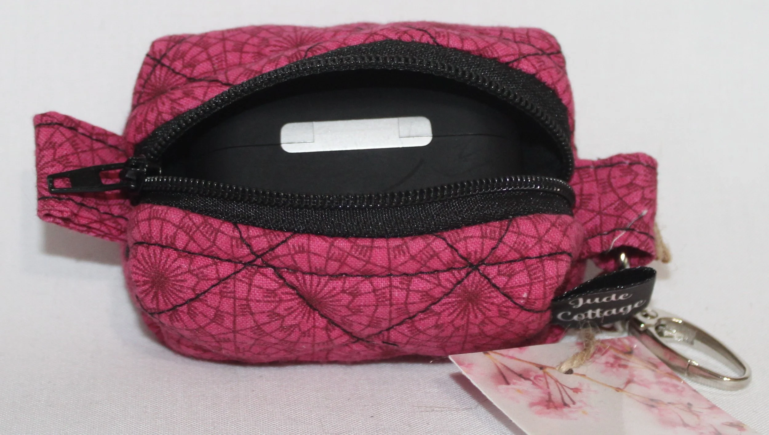 Front view of the Claire Bag Charm featuring a dark pink fabric with geometric print shown with an Airpod Pro earbud case inserted to show sizing.