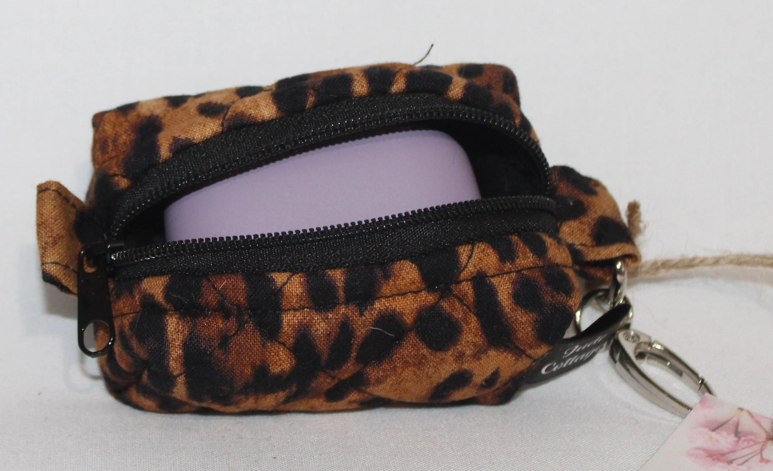 Top open view of the Lyra Bag Charm featuring a leopard print fabric and shown with a J Lab earbud case inserted for sizing reference.