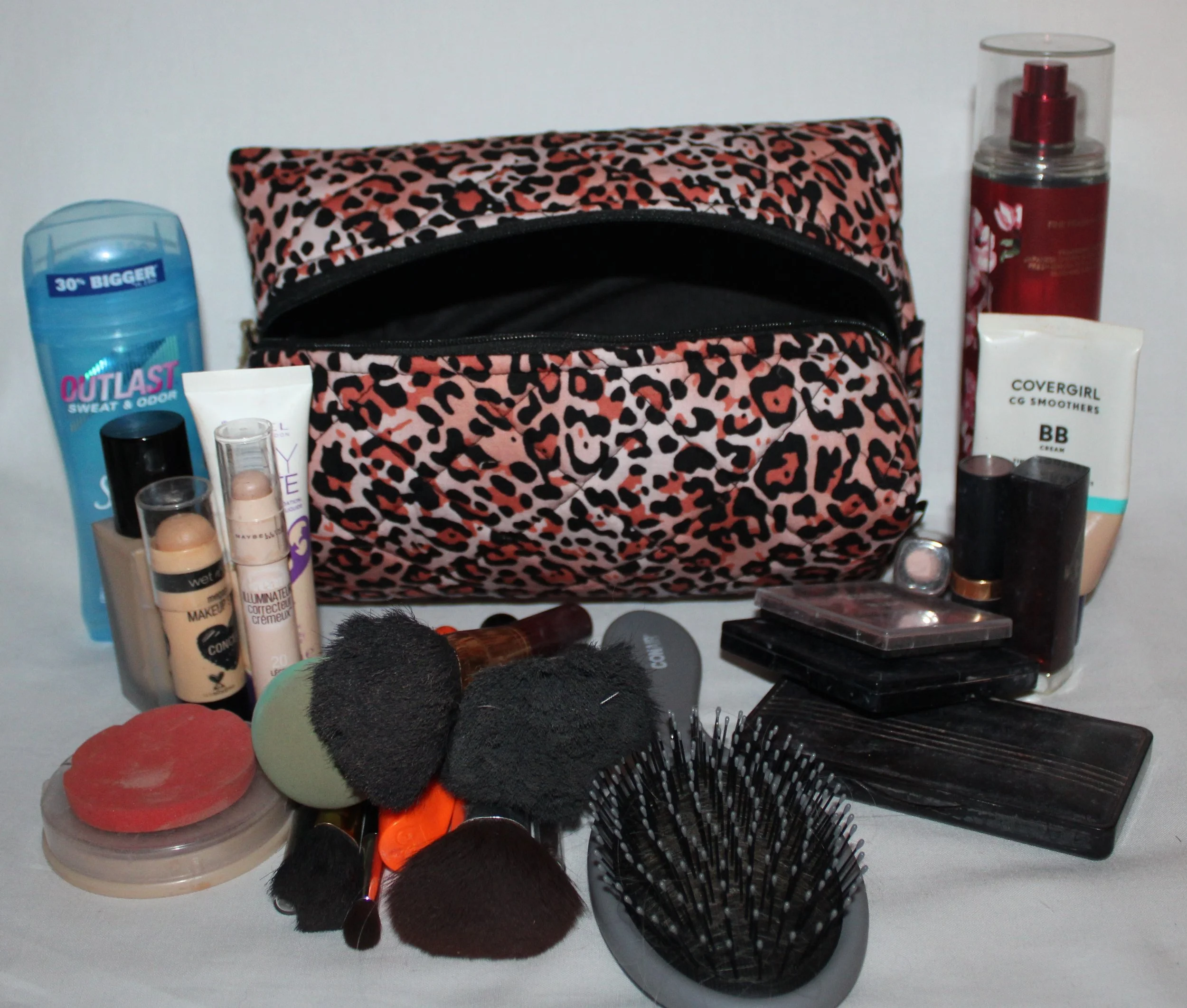 Open‑top view of the large Mia quilted travel pouch in pink leopard print with assorted cosmetics arranged around it.