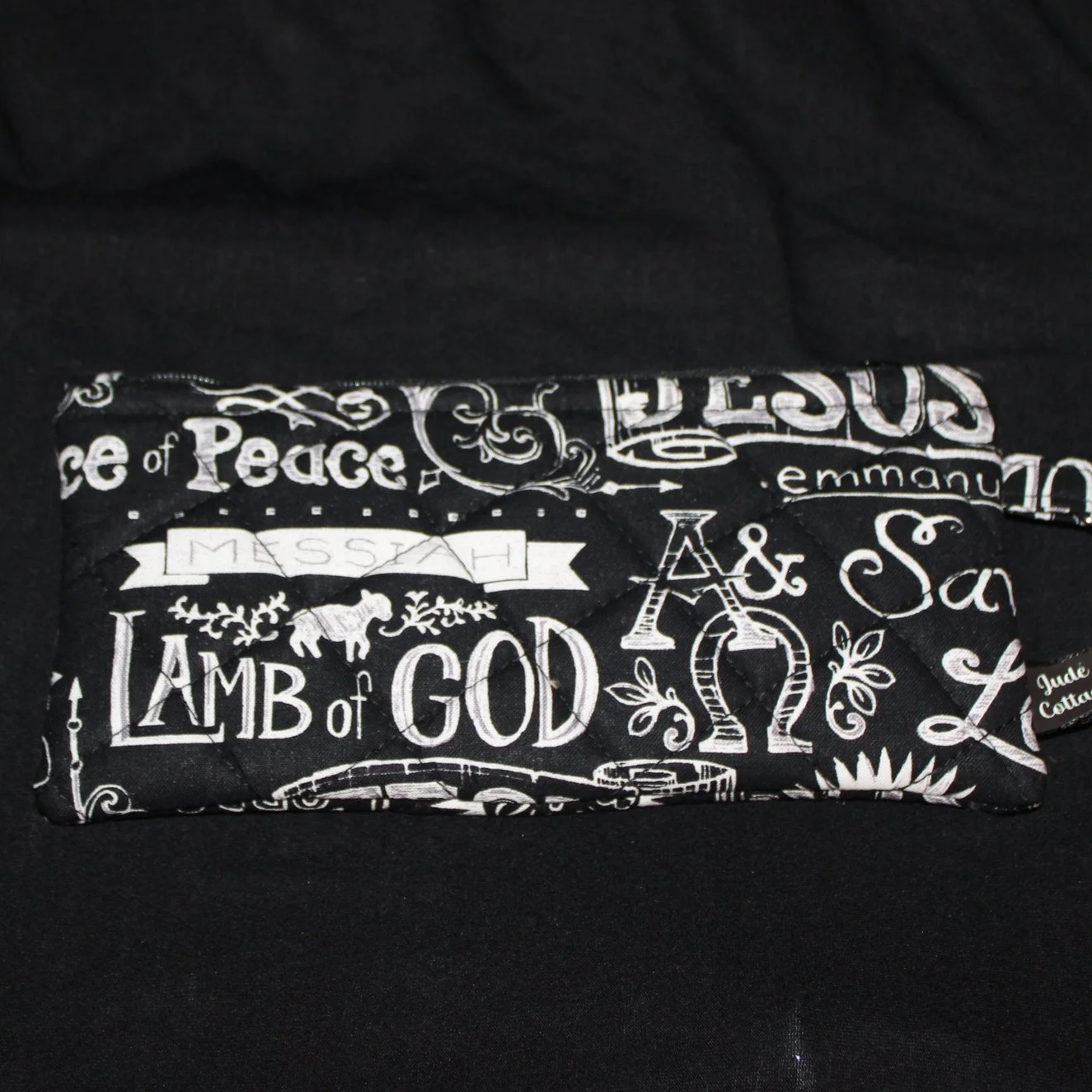 Front flat view of the King of Kings Large Keychain Wallet featuring the names of Jesus on black fabric with white font.