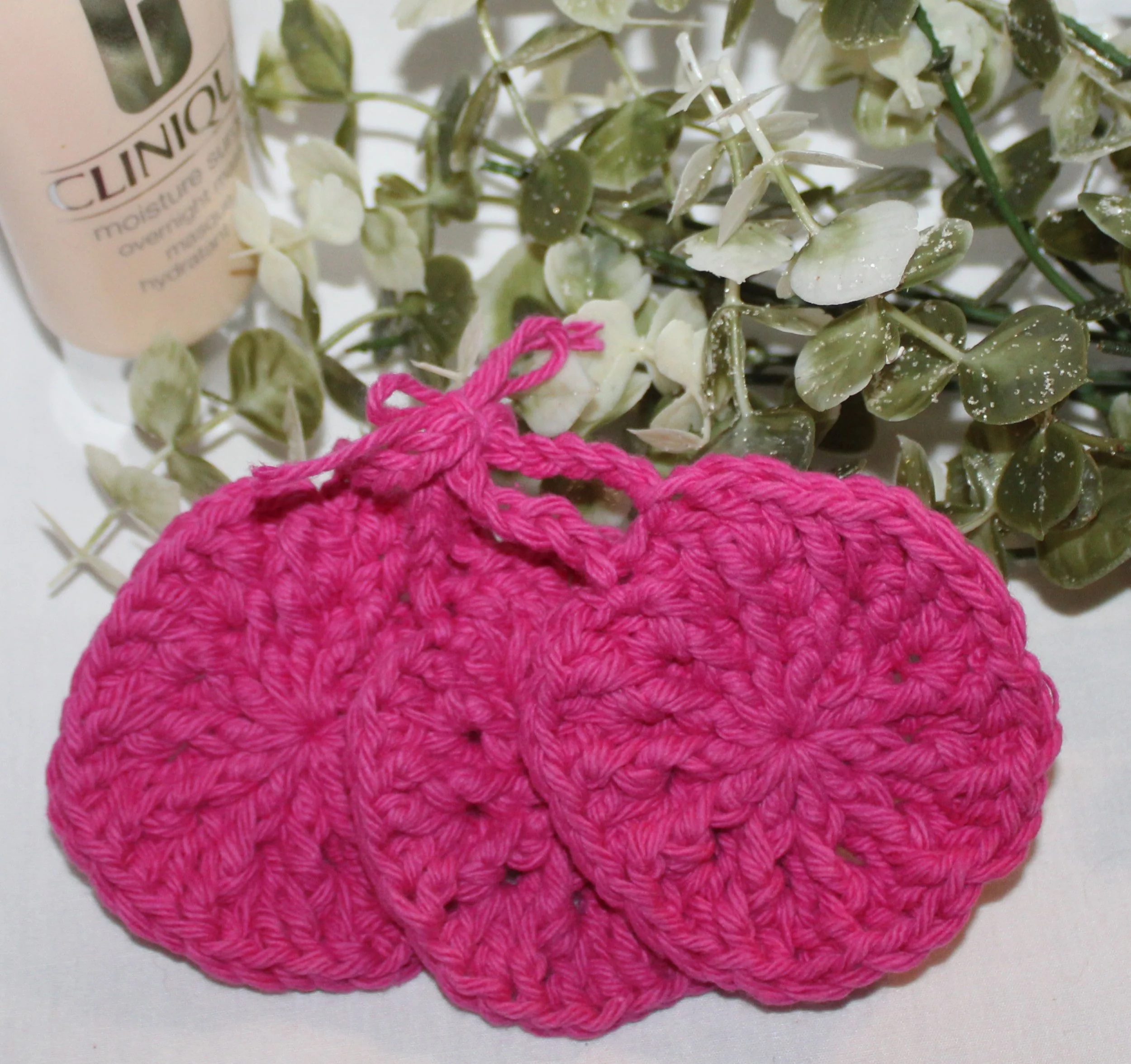 Close‑up of set of three round crocheted fuchsia facial scrubbies with a textured stitch pattern.