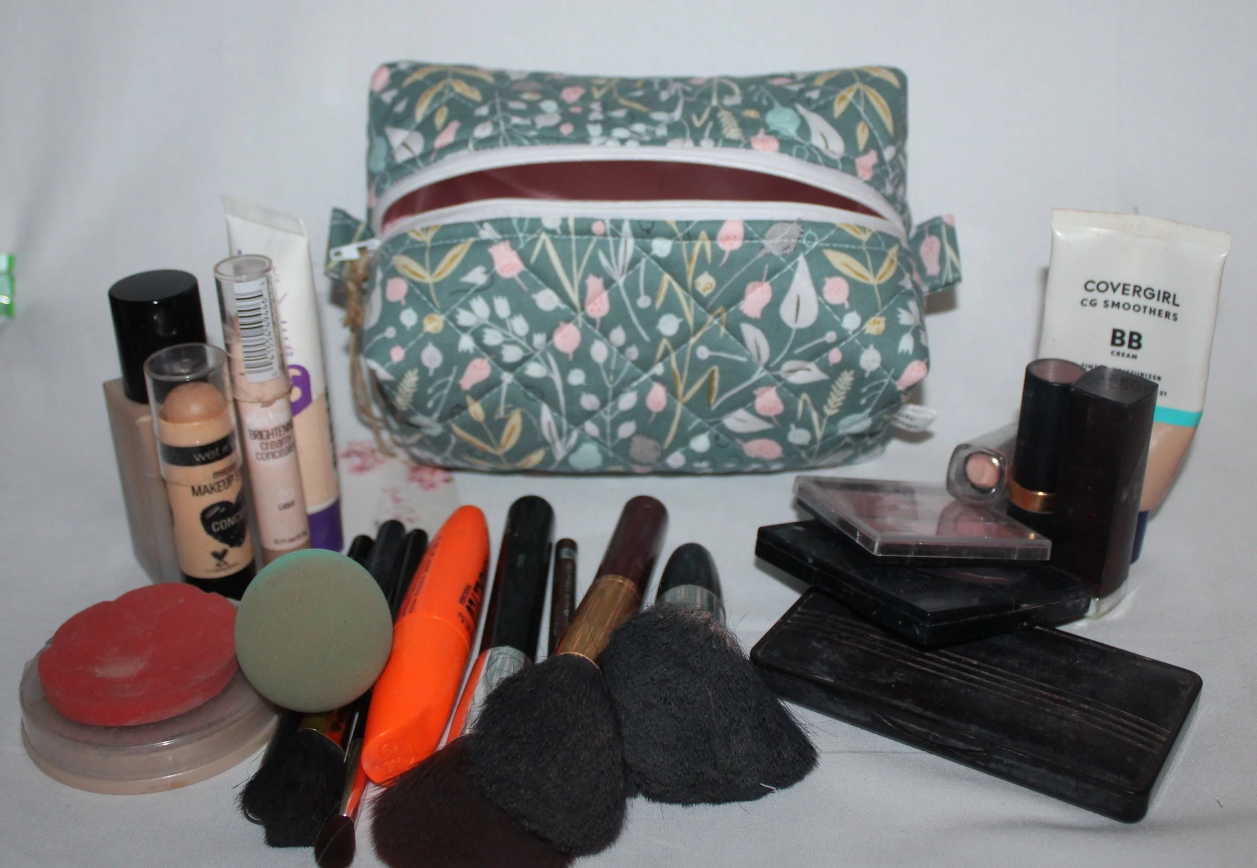 Top view of the open small Meadow Breeze green floral quilted travel pouch with the empty interior visible and makeup items placed around it for scale.