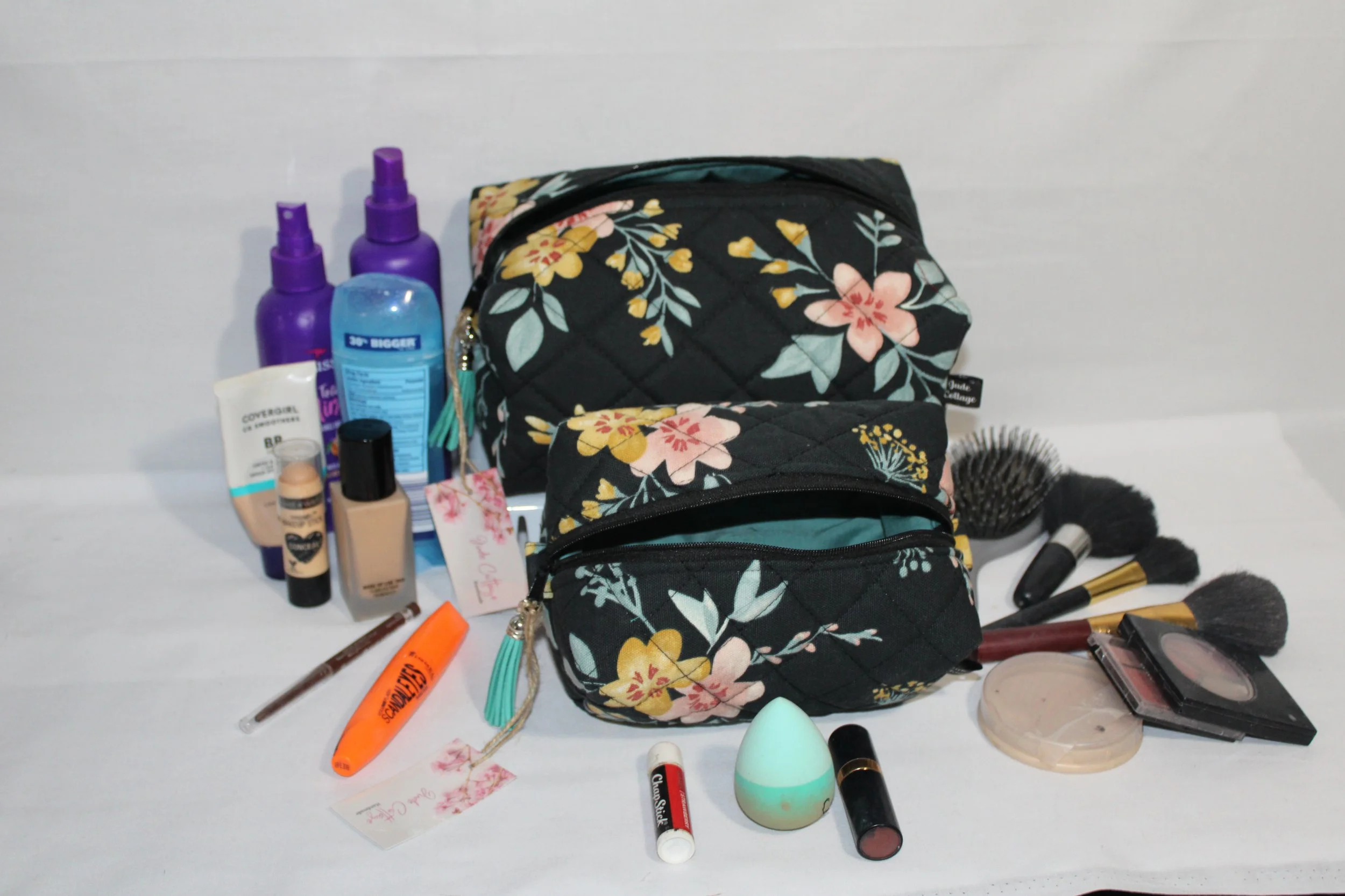 Large and small Twyla quilted travel pouches in floral print displayed with cosmetics and hygiene products arranged around them to show size.