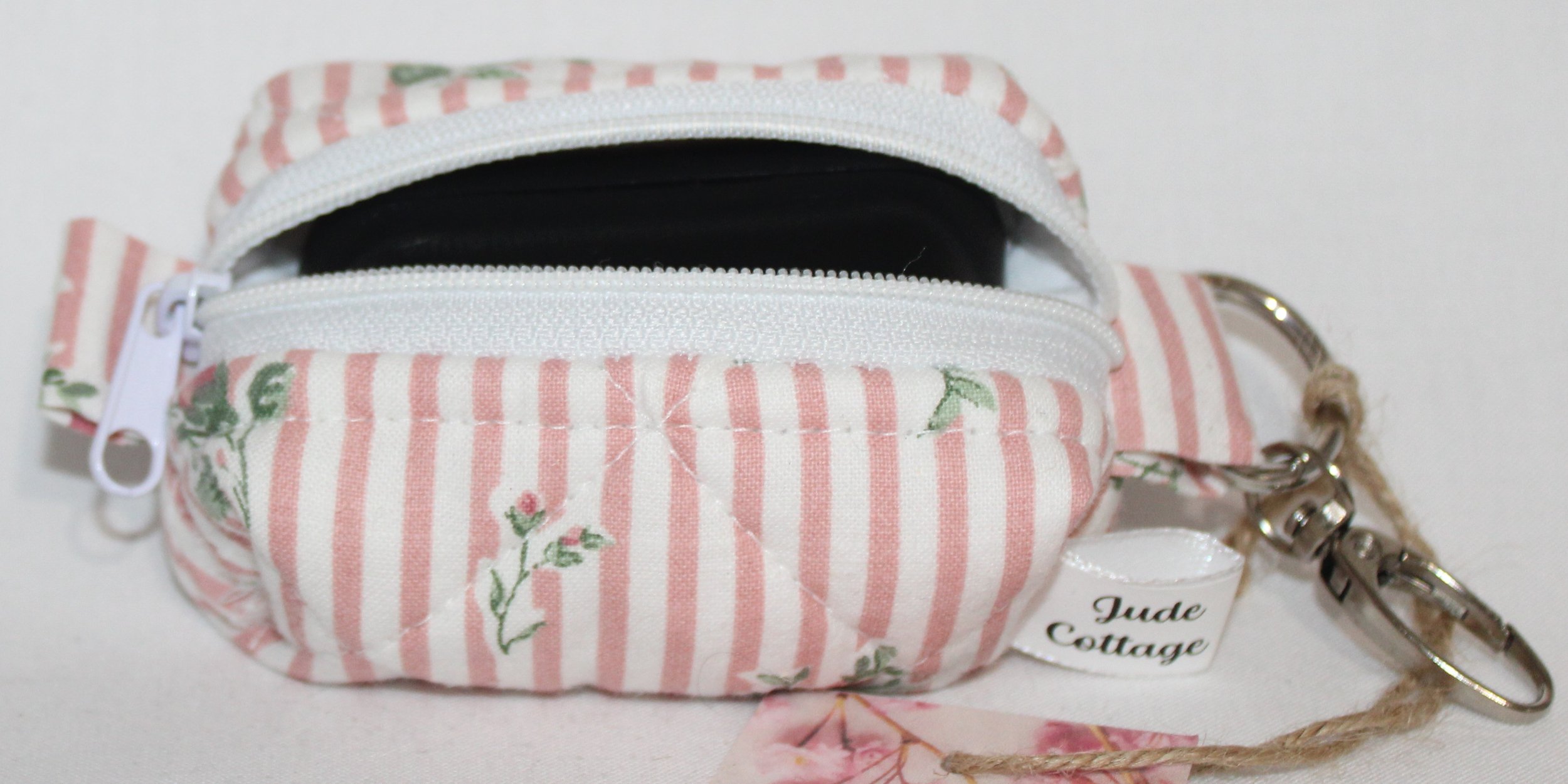 Open top view of the Victoria bag charm featuring pink and white stripes with pink rose bud printed fabric shown with a set of J Lab earbuds inserted for sizing reference.