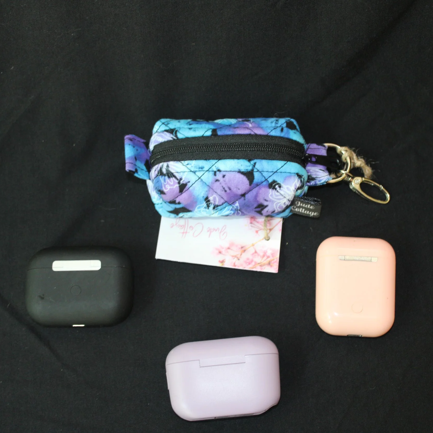 Top closed view of the Butterfly Mist Bag Charm showing black zip enclosure and pictured with three different sized earbuds for sizing referendce.