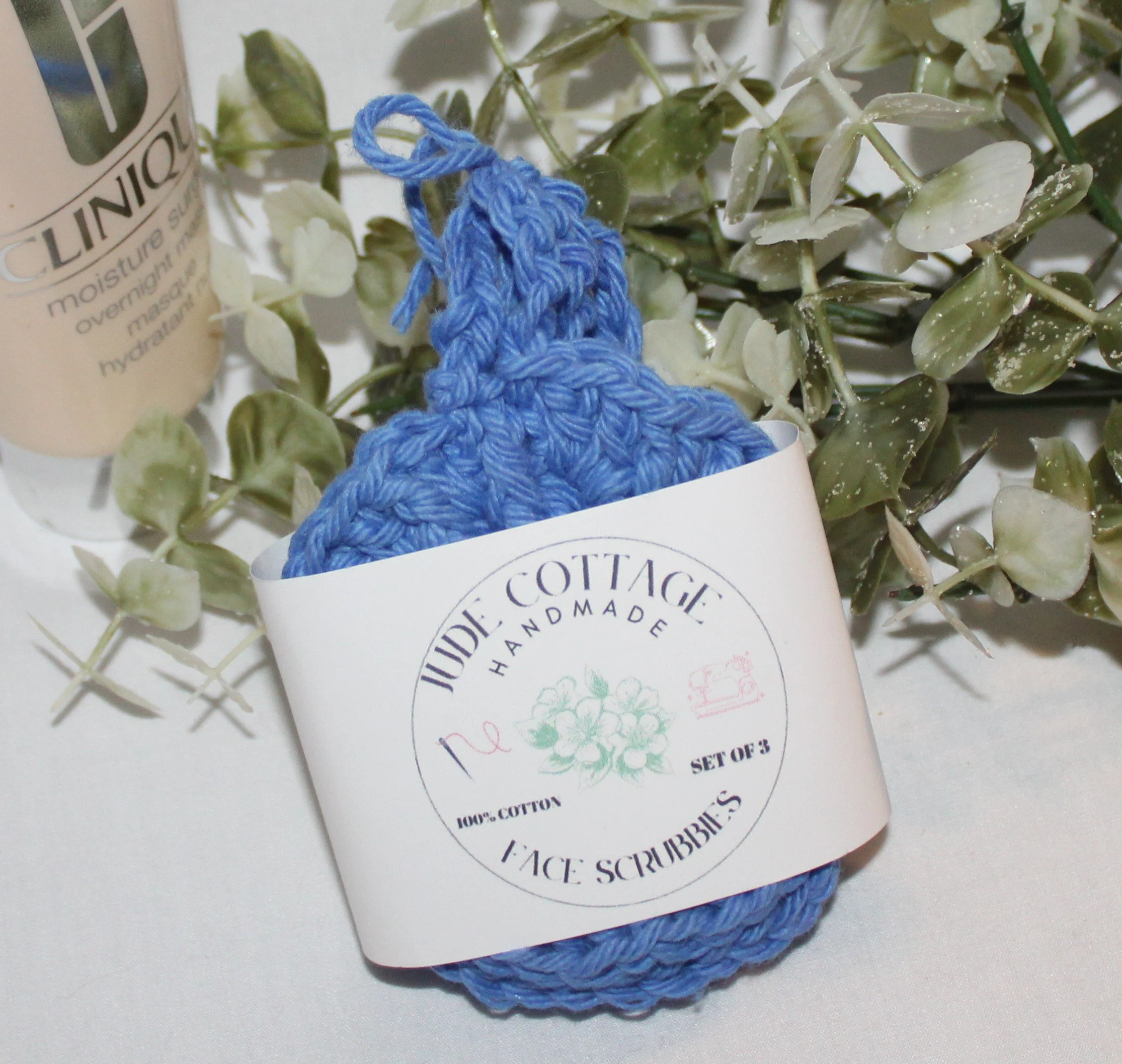 Close‑up of set of three round crocheted royal blue facial scrubbies with a textured stitch pattern shown with label.