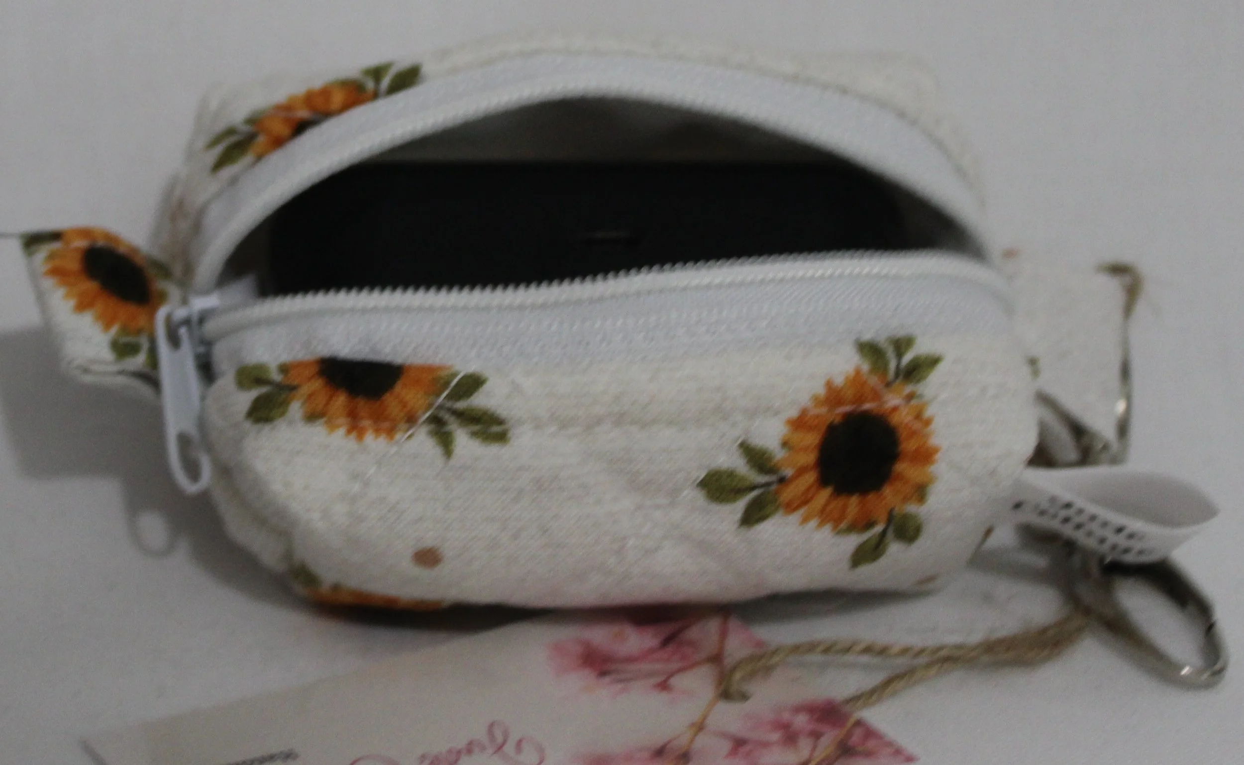 Open top view of the Sunflower Medley Bag Charm featuring small sunflowers on a cream background shown with a set of J Lab earbuds inserted for size demonstration.