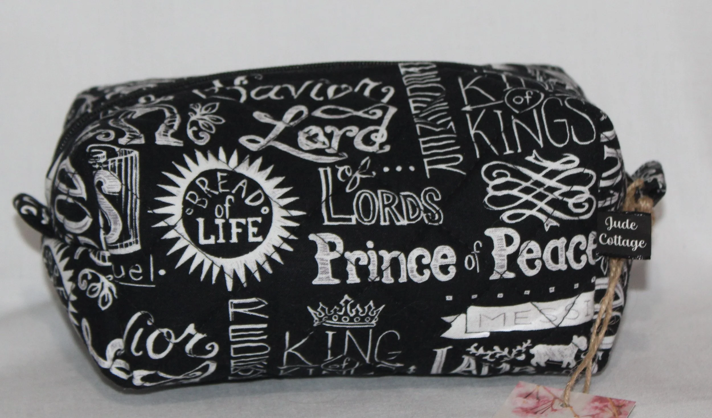 Front view of the King of Kings quilted travel pouch with black fabric and white names‑of‑Jesus print.
