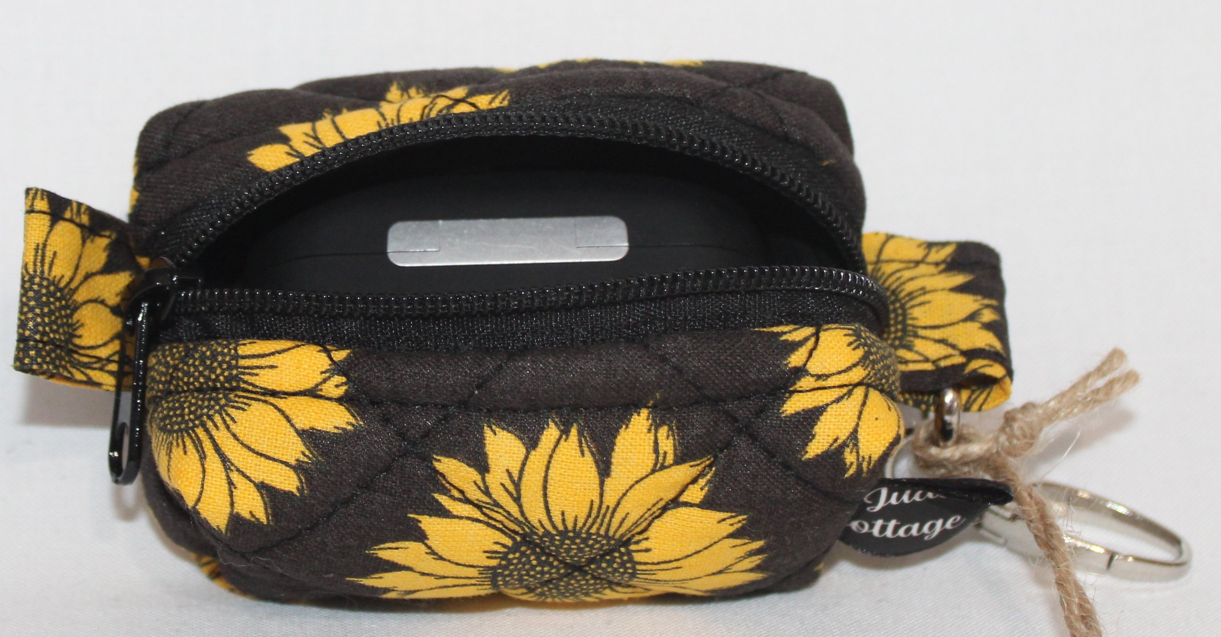 Top open view of the Midnight Sunflower Bag Charm featuring a black background fabric with bright golden yellow sunflowers, shown with an Airpod Pro case inserted to demonstrate fit.