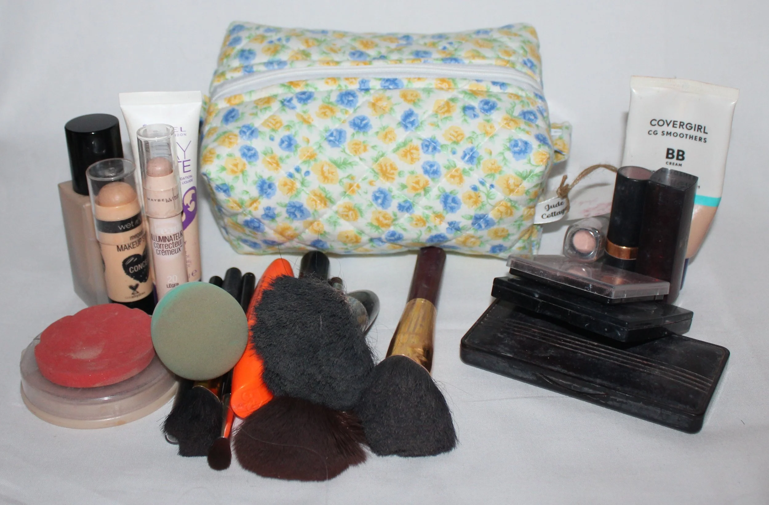 Front view of the small Melody quilted travel pouch in blue and yellow floral print with cosmetics arranged in front to show size.