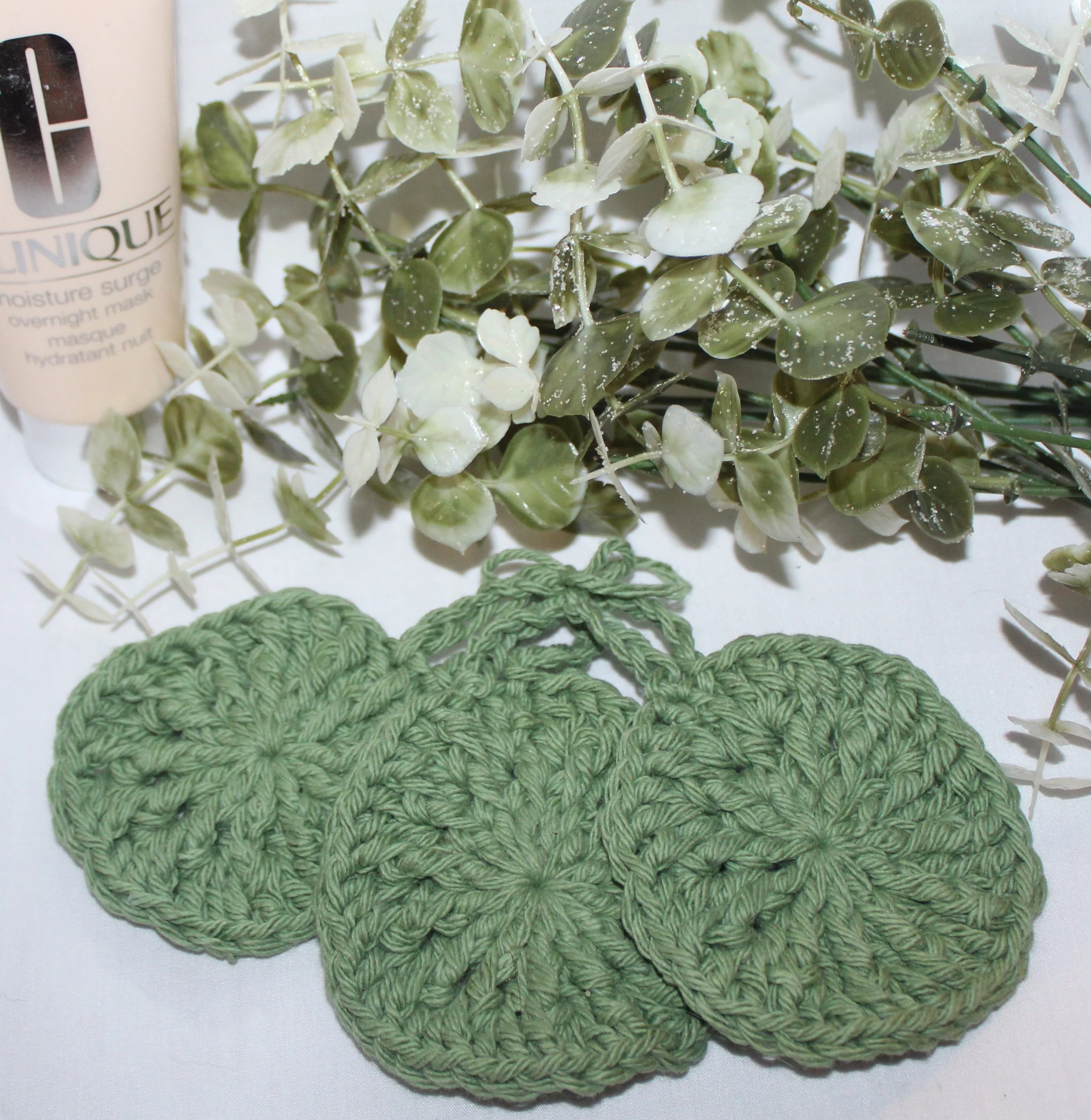 Close‑up of set of three round crocheted sage green facial scrubbies with a textured stitch pattern.