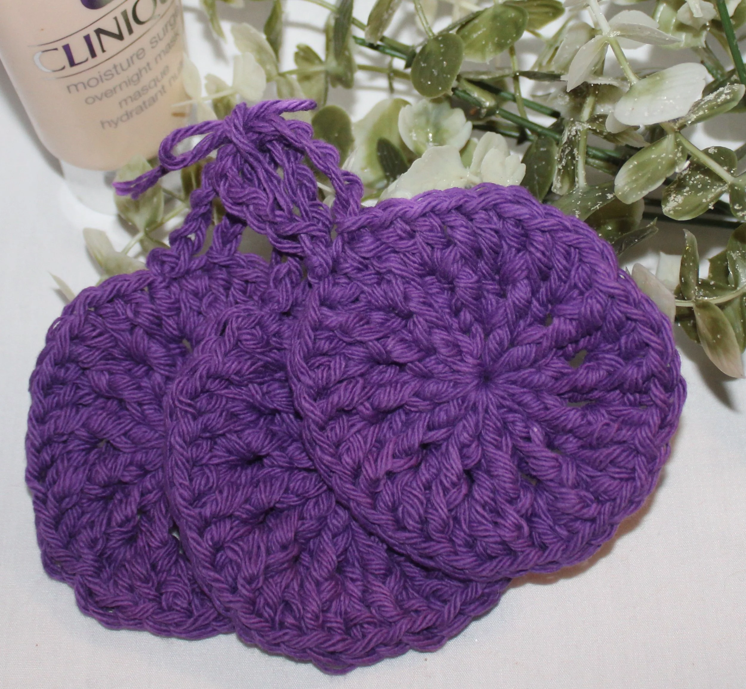 Close‑up of set of three round crocheted plum facial scrubbies with a textured stitch pattern.