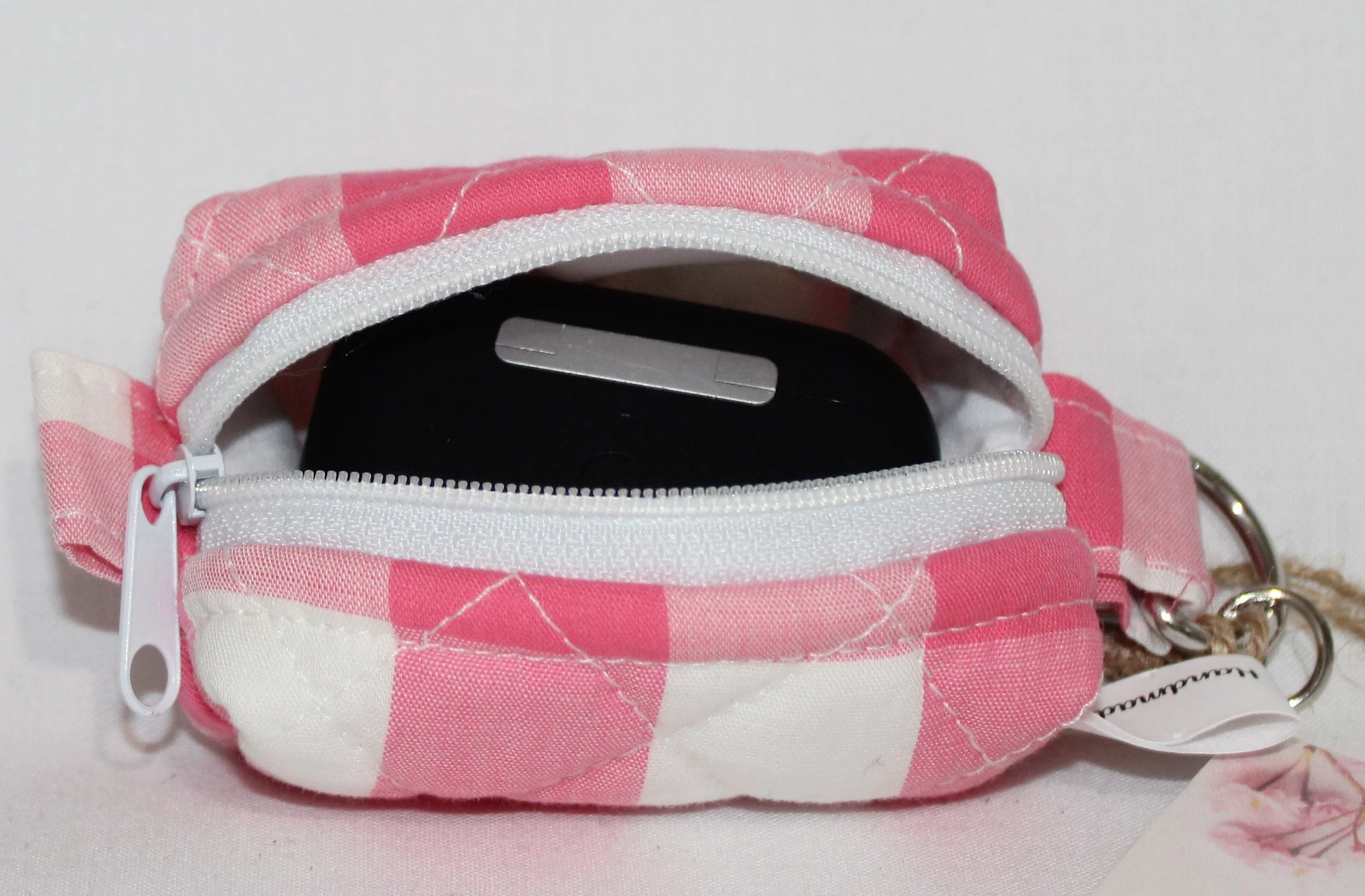 Top open view of the Sophie Bag Charm featuring a pink and white check fabric shown with an Airpod Pro earbud case inserted to demonstrate sizing.