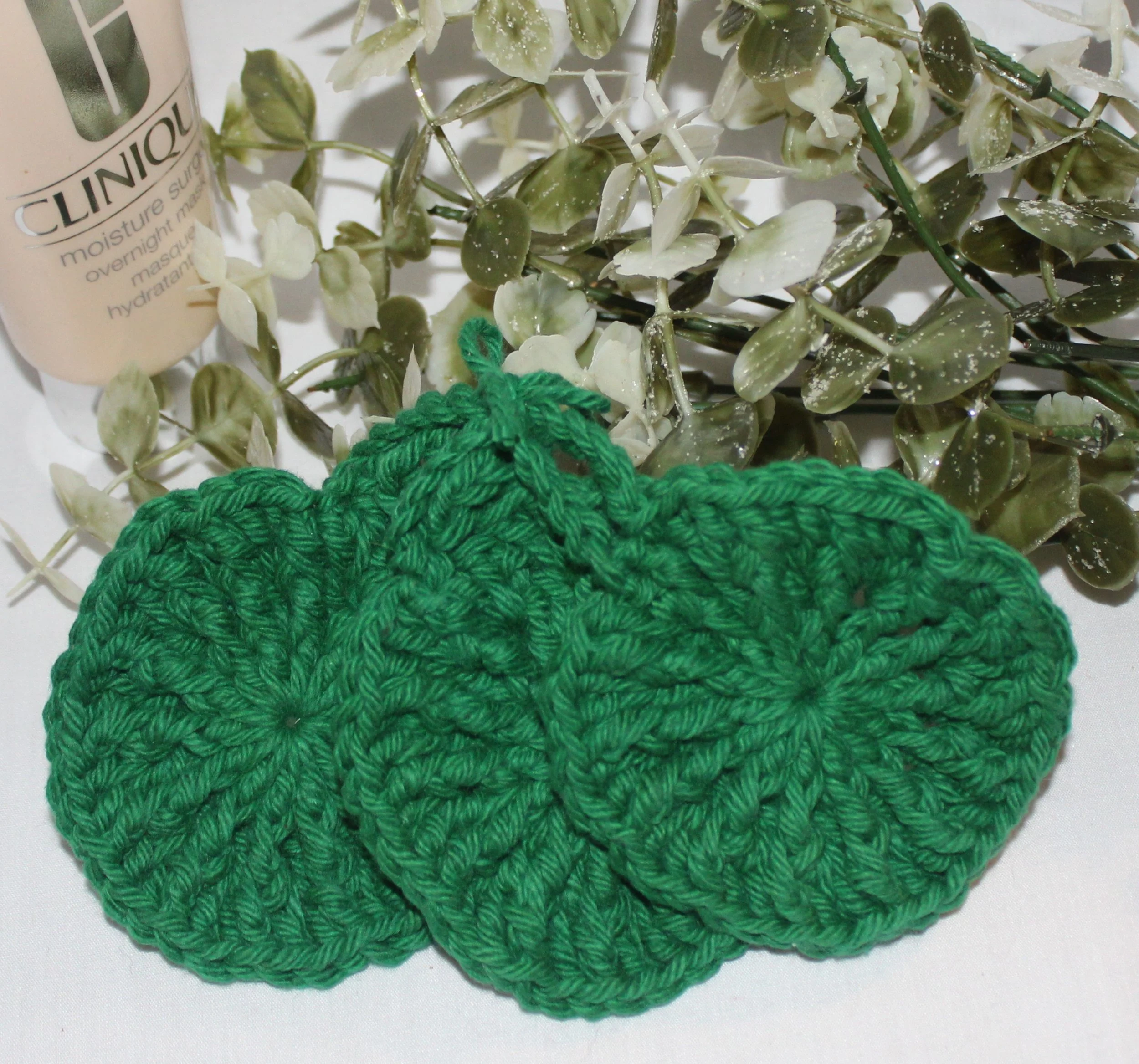 Close‑up of set of three round crocheted green facial scrubbies with a textured stitch pattern.