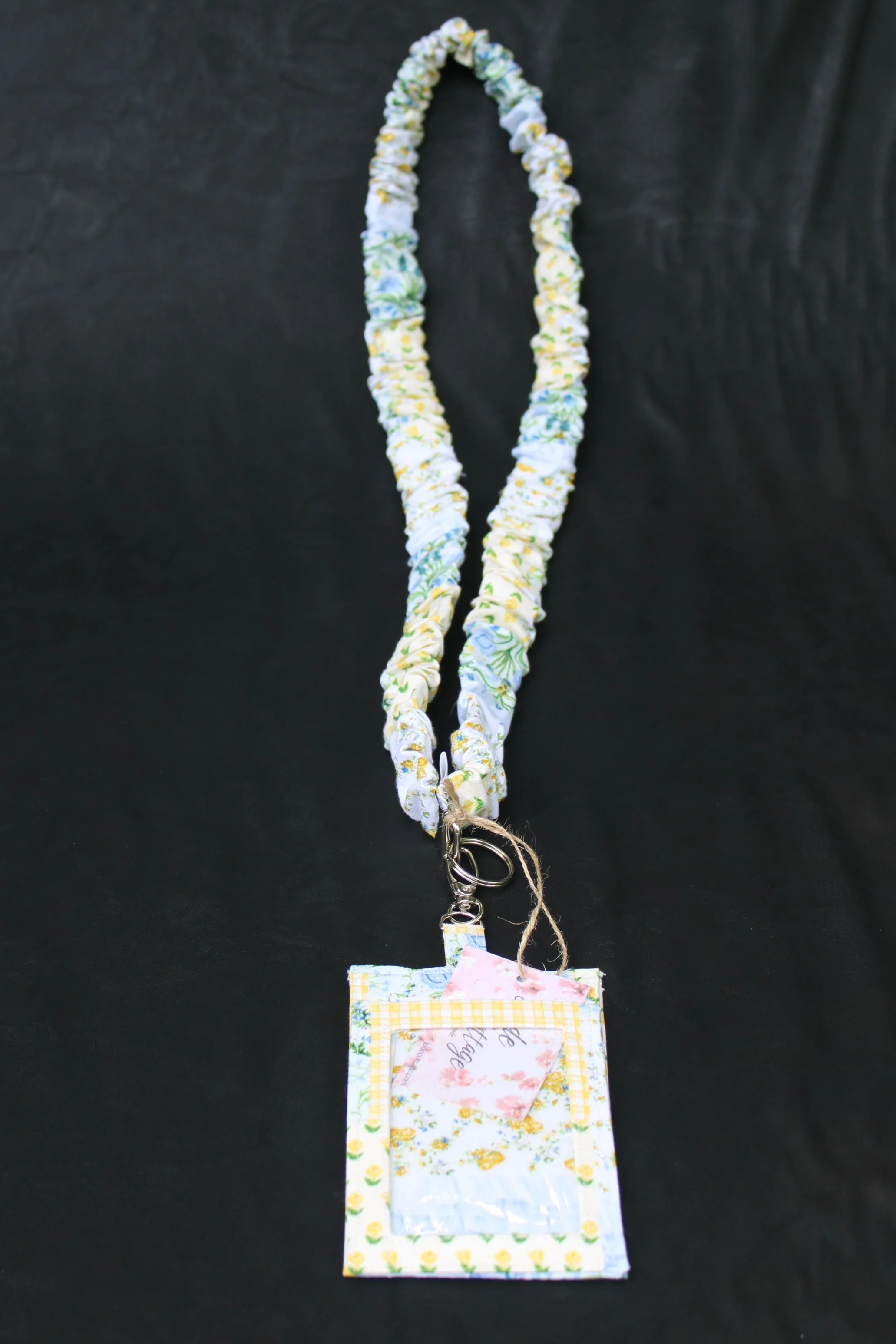 Front view of the Annalee Scrunch Lanyard with Badge holder featuring a blue, yellow, white, and green floral patchwork print, shown with a card partially inserted in the clear ID pocket.