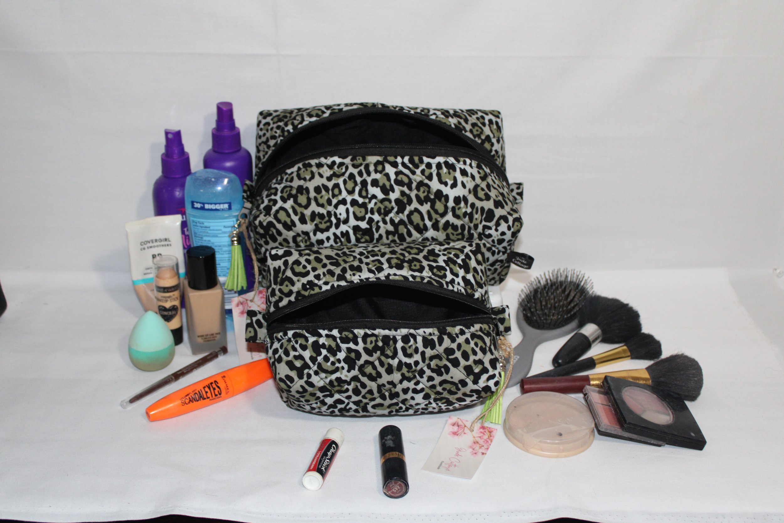 Angled front view of both large and small Diana quilted travel pouch shown with cosmetics to illustrate size.