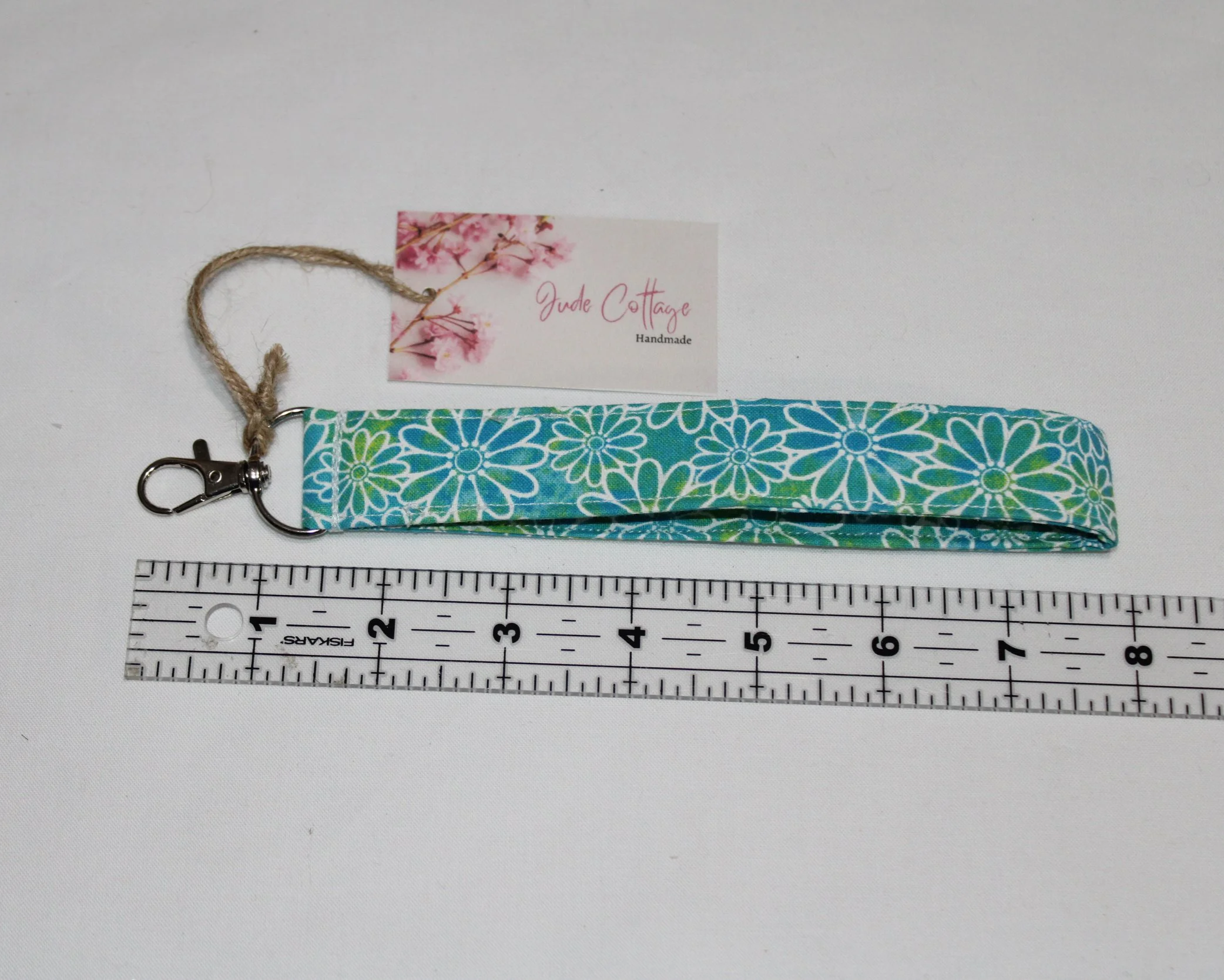 Neon Daisy Wristlet made from bright multicolor daisy‑print fabric with an approximately 7.5‑inch strap, metal clasp, and branded tag, displayed with a ruler to show size.