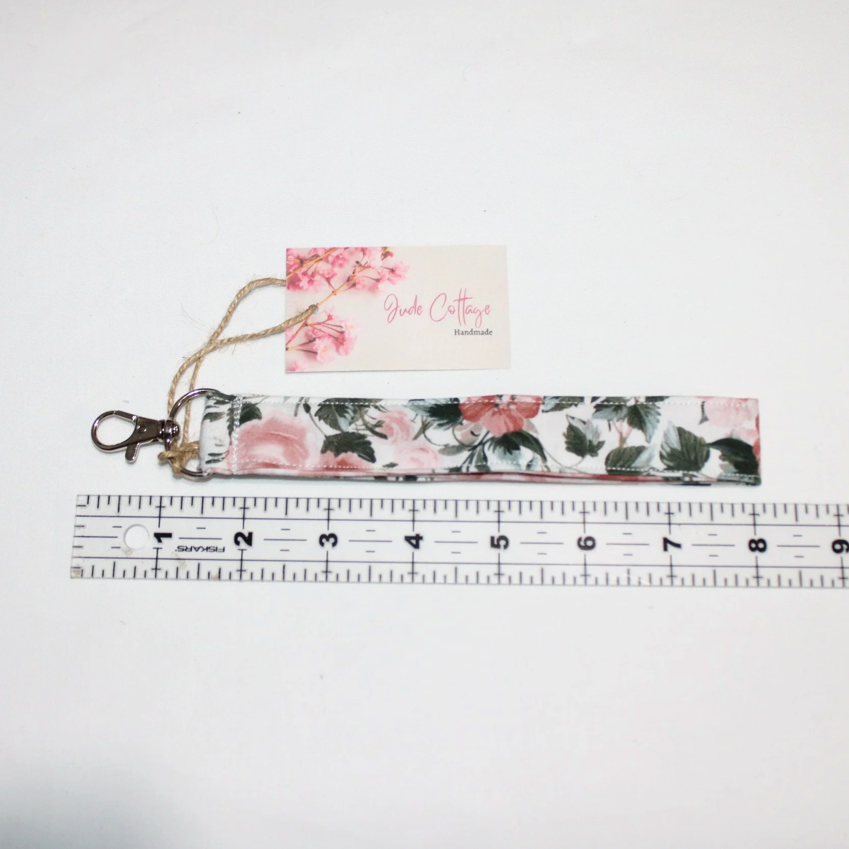 Up close view of the Rose Garden wristlet showing a white background with pink roses and greenery, above a ruler illustrating size,
