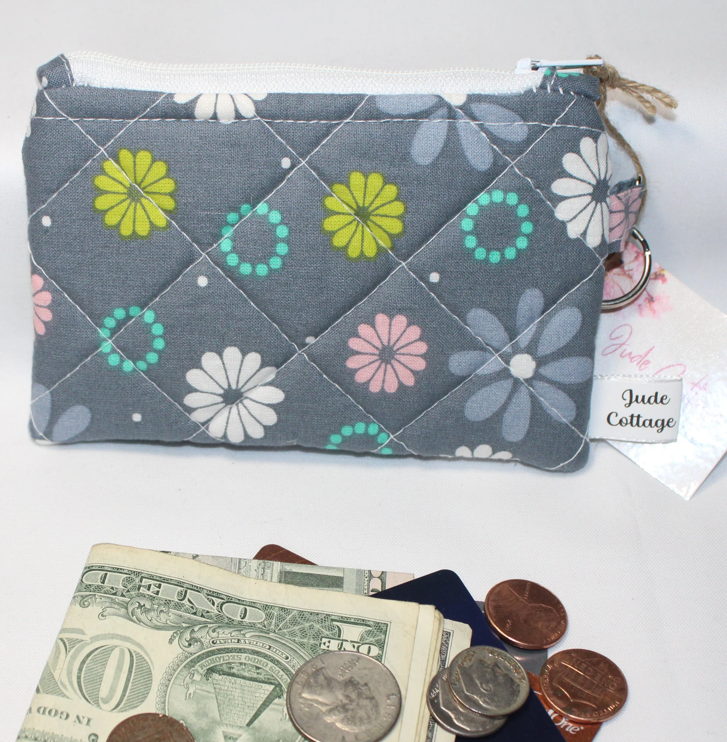 Front view of the Phoebe quilted keychain wallet with soft modern pattern, zipper closure, and metal key ring shown with cash, cards, and coins to show use.