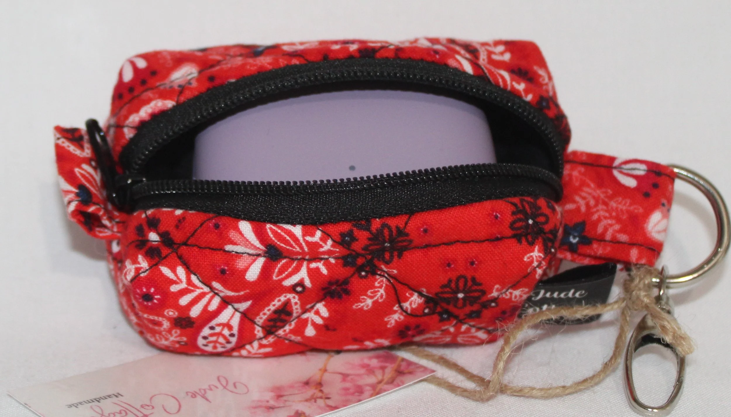Top open view of the Freedom Red Bag Charm featuring red background with floral and paisley print fabric, shown with a J Lab earbud case inserted to demonstrate fit.