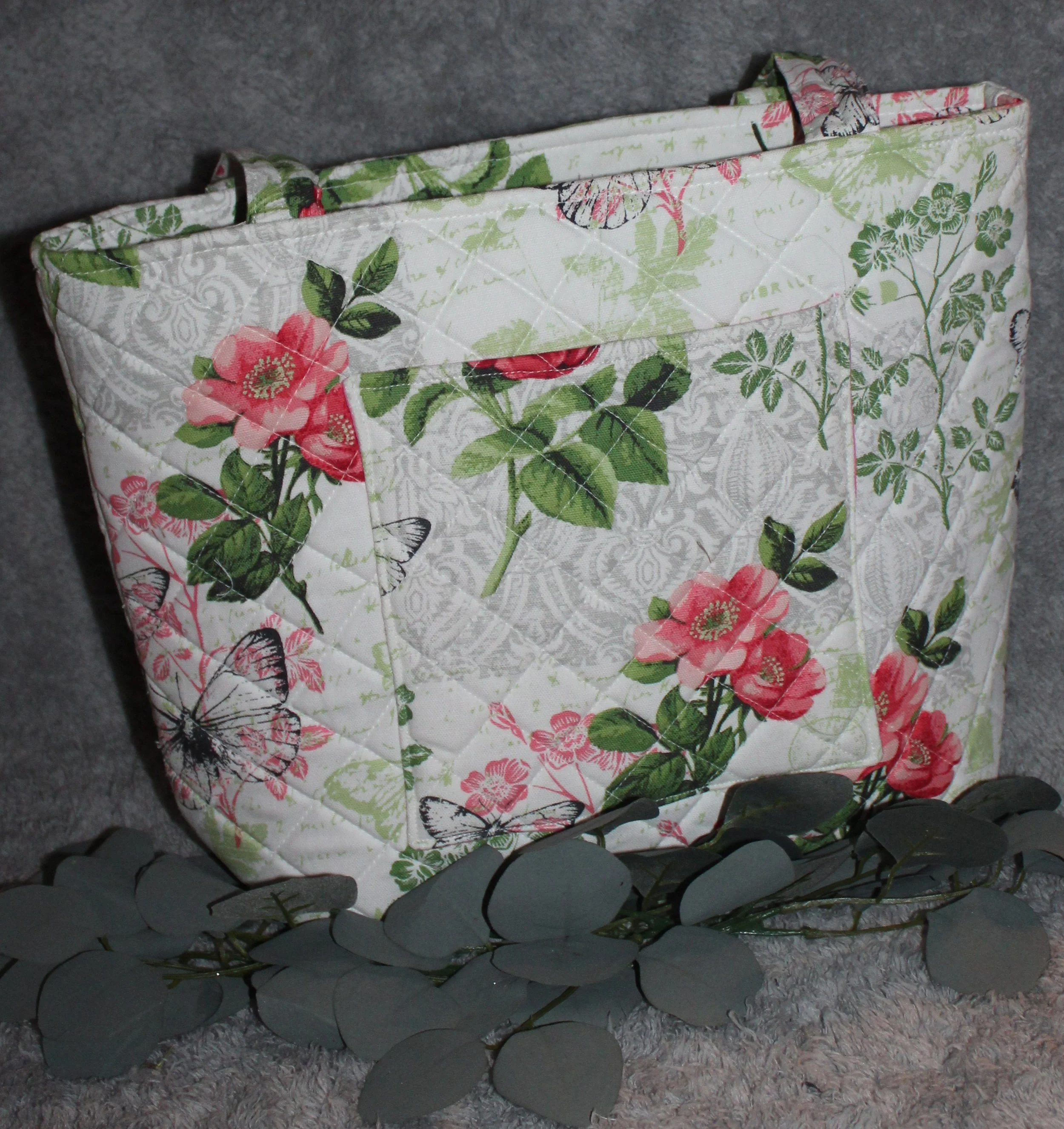 Back view of the Colette quilted tote in white fabric with a pink floral pattern, showing the quilted exterior, two padded shoulder straps, and one exterior slip pocket.