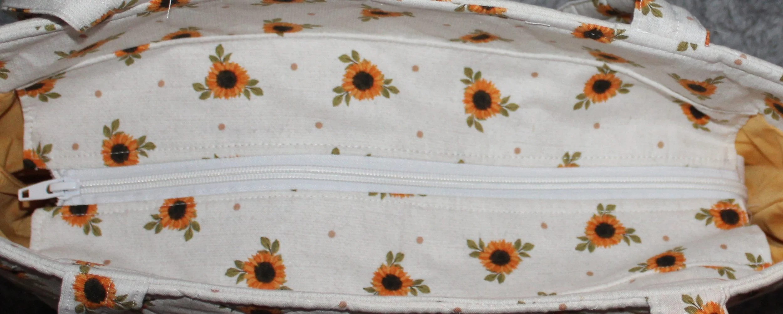 Top view of the Sunflower Medley quilted tote in white fabric with a dainty sunflower floral pattern, shown with the recessed zipper fully closed.
