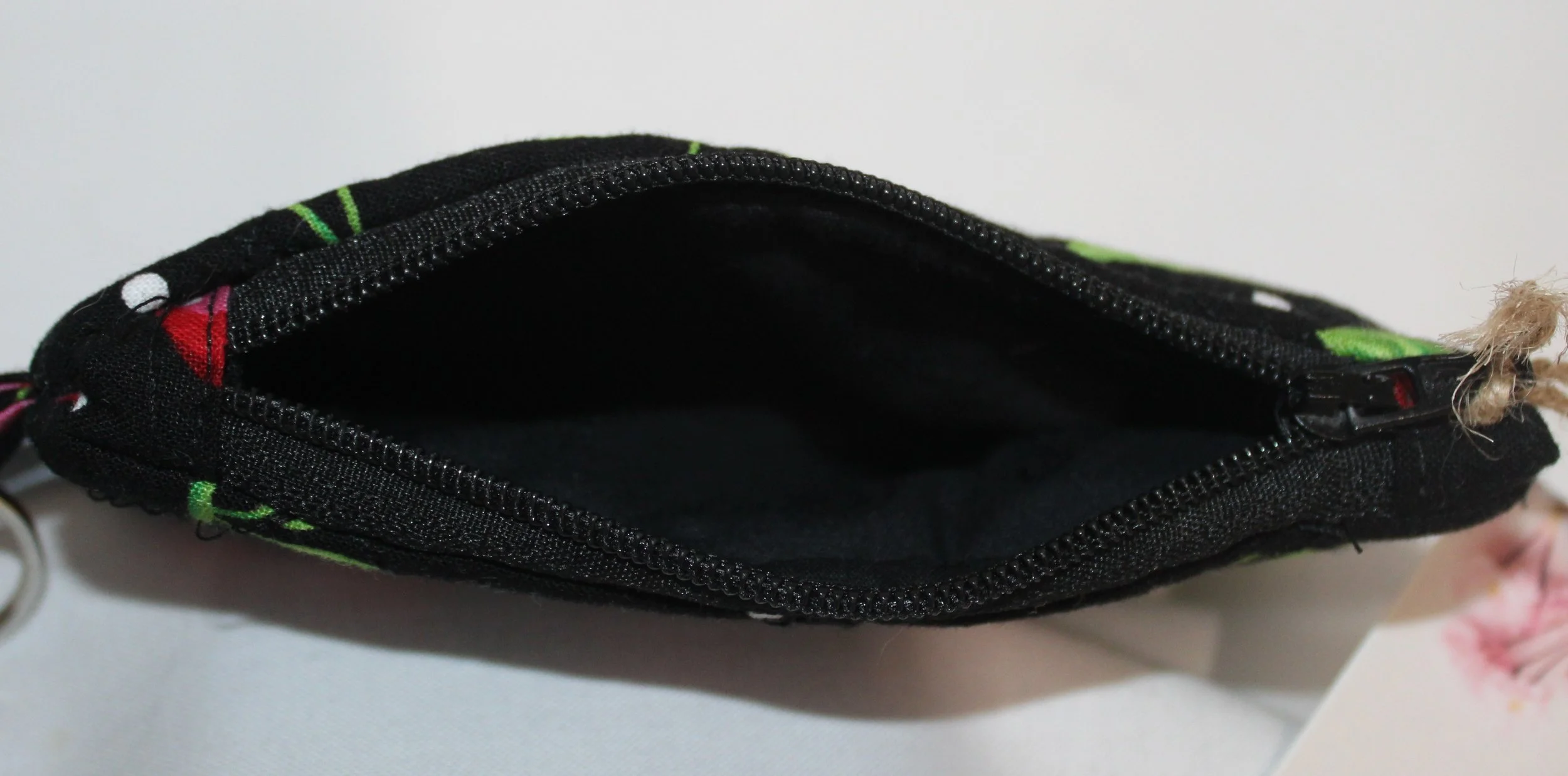 Top view of a small, zippered keychain wallet featuring red cherries and green leaves on black fabric, showing black interior.