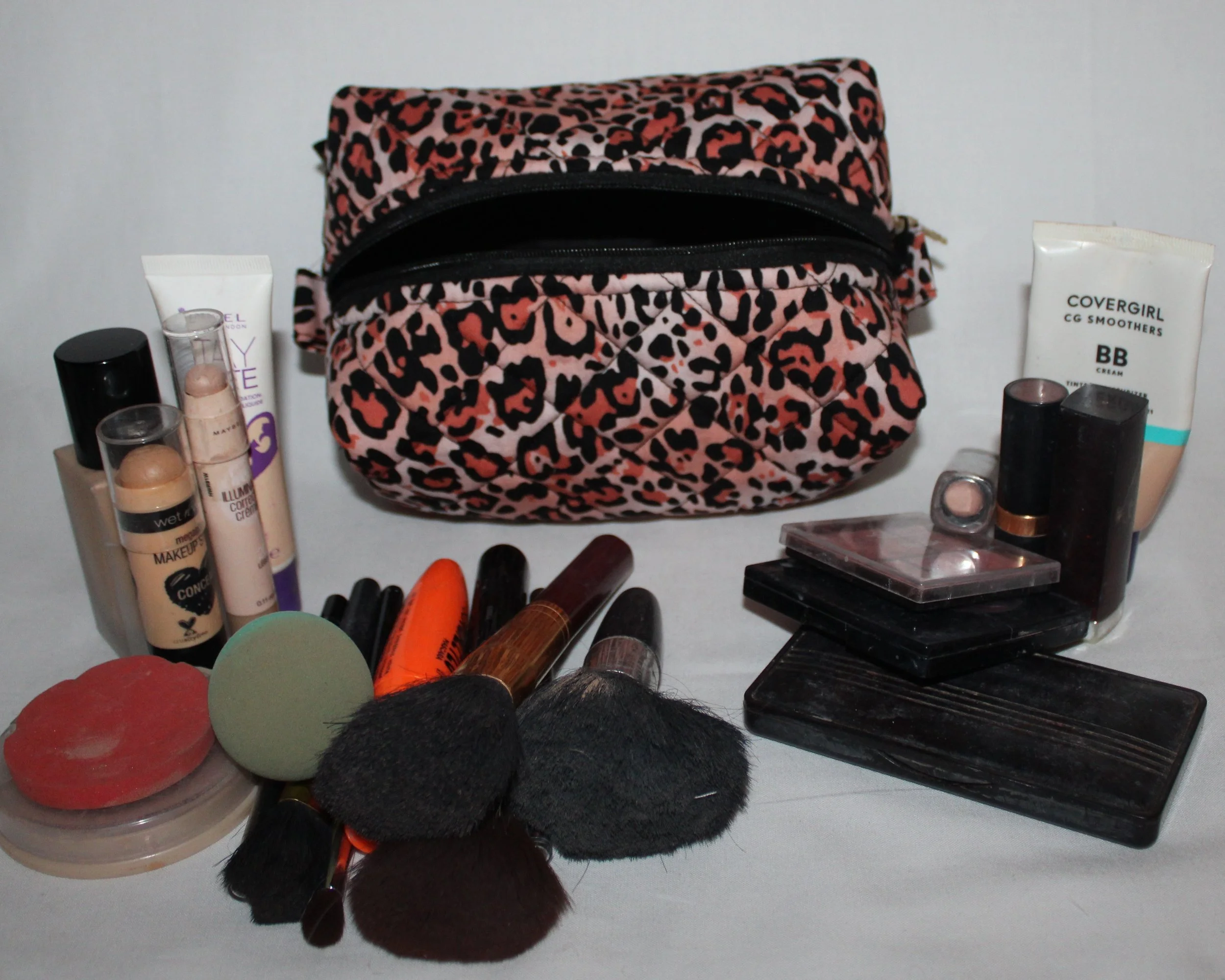 Open-top view of the small Mia quilted travel pouch in pink leopard print with assorted cosmetics arranged around it.