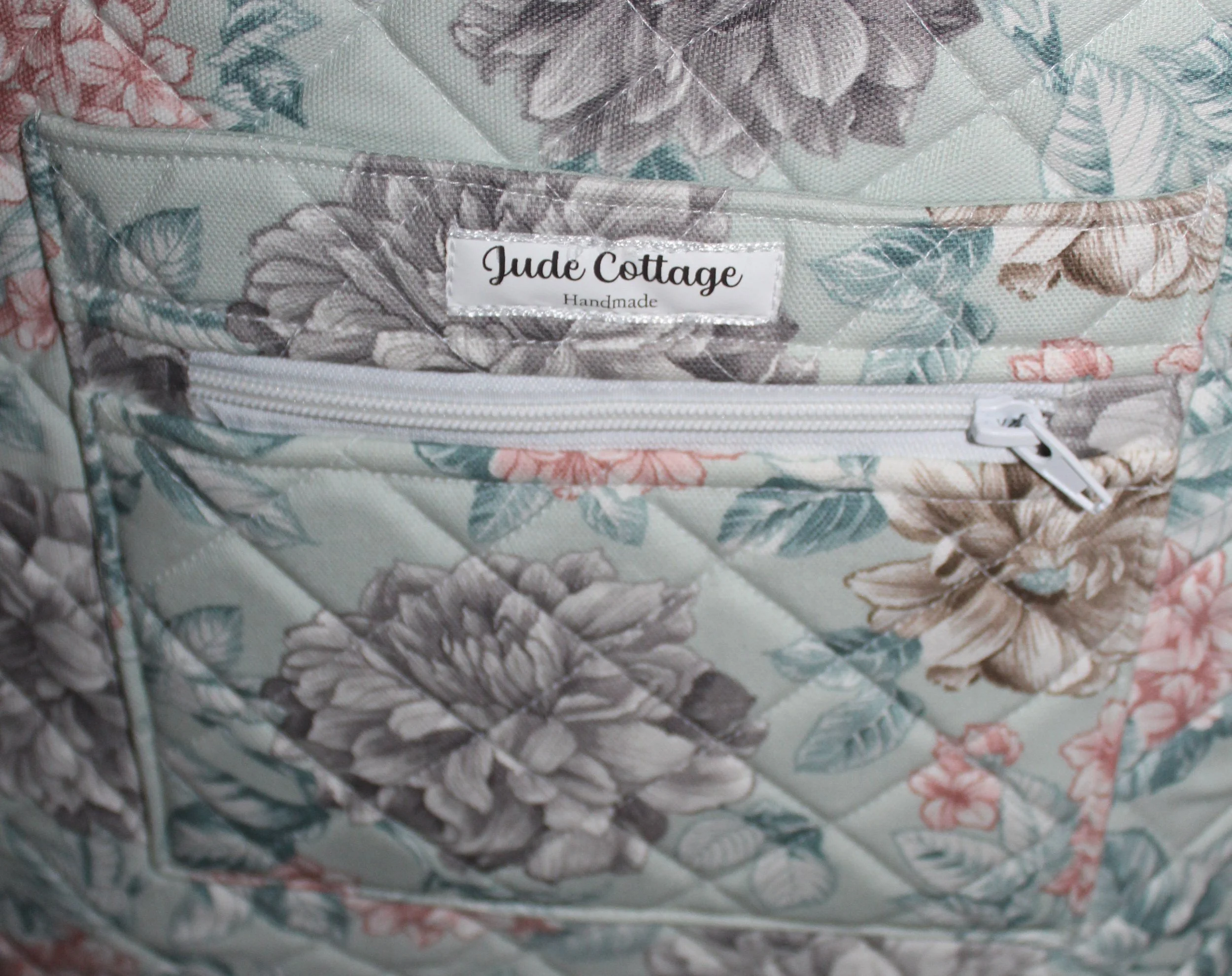 Up‑close view of the front pockets of the Joelle quilted tote, showing one exterior slip pocket and one exterior zip pocket, along with the quilted pattern.