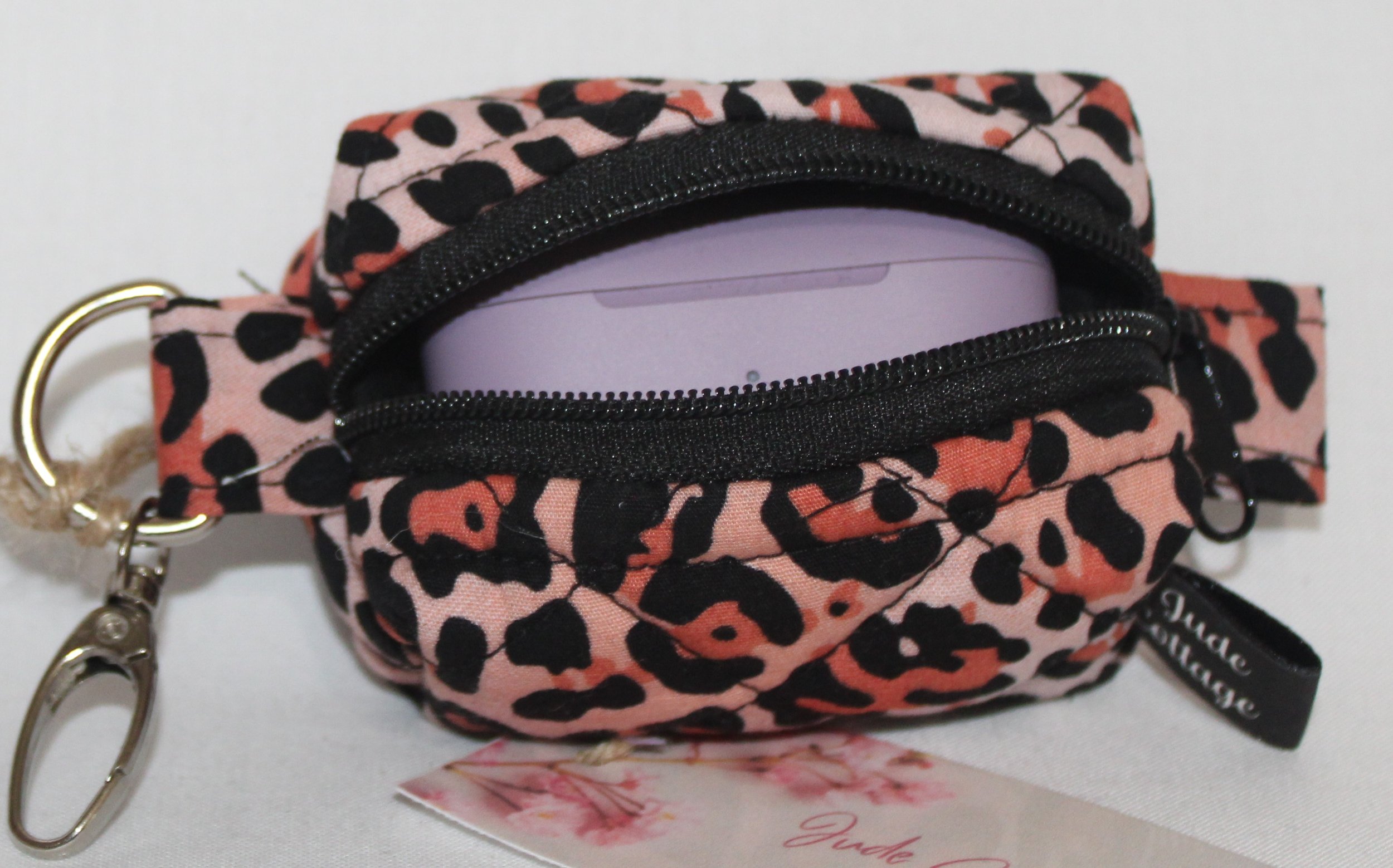 Top open view of the Mia Bag Charm featuring pink leopard print fabric shown with a set of J Lab earbuds inserted for sizing reference..