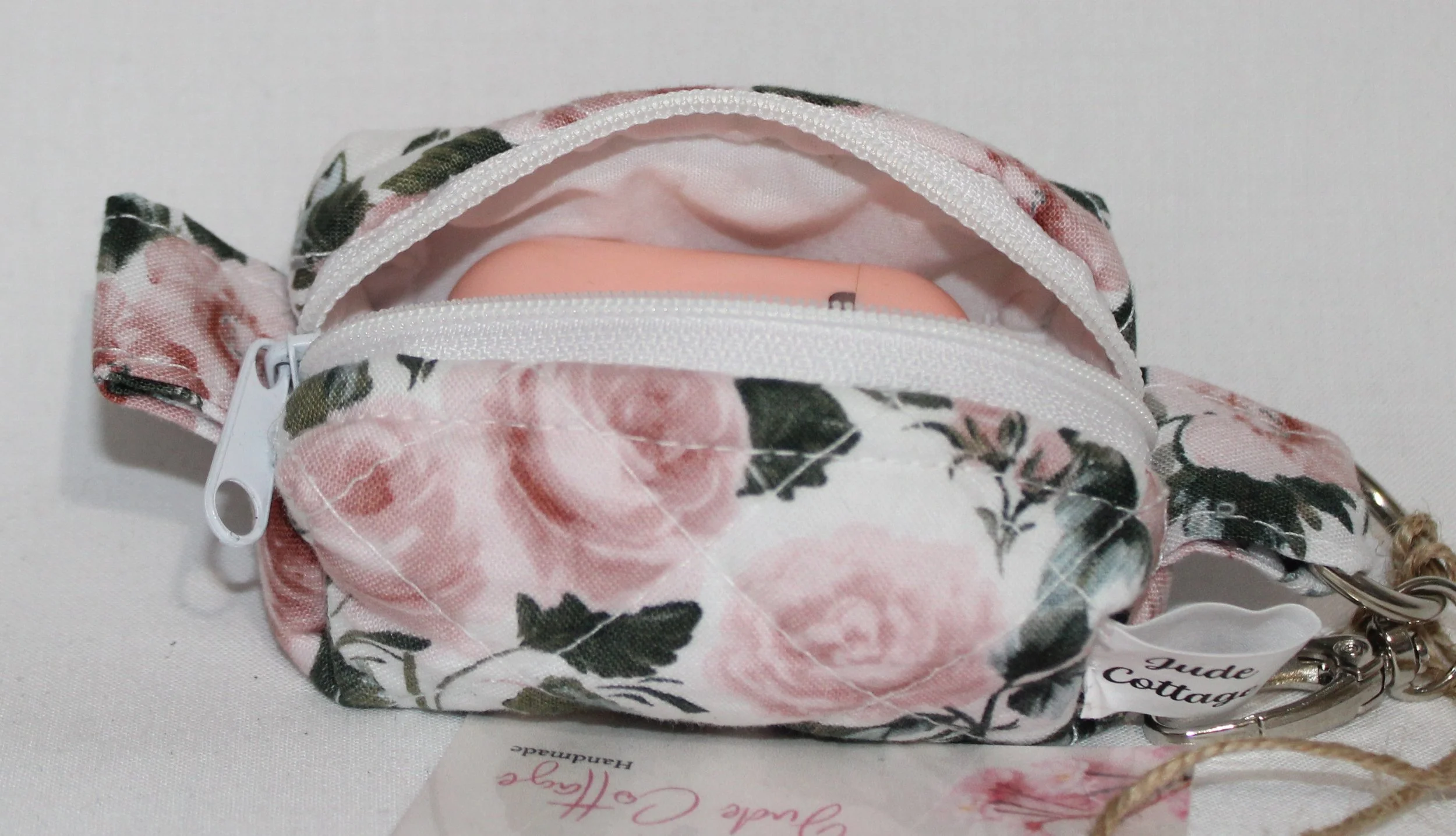 Open top view of the Rose Garden Bag Charm featuring white fabric with pink rose print shown with an Airpod earbud case inserted for size reference.