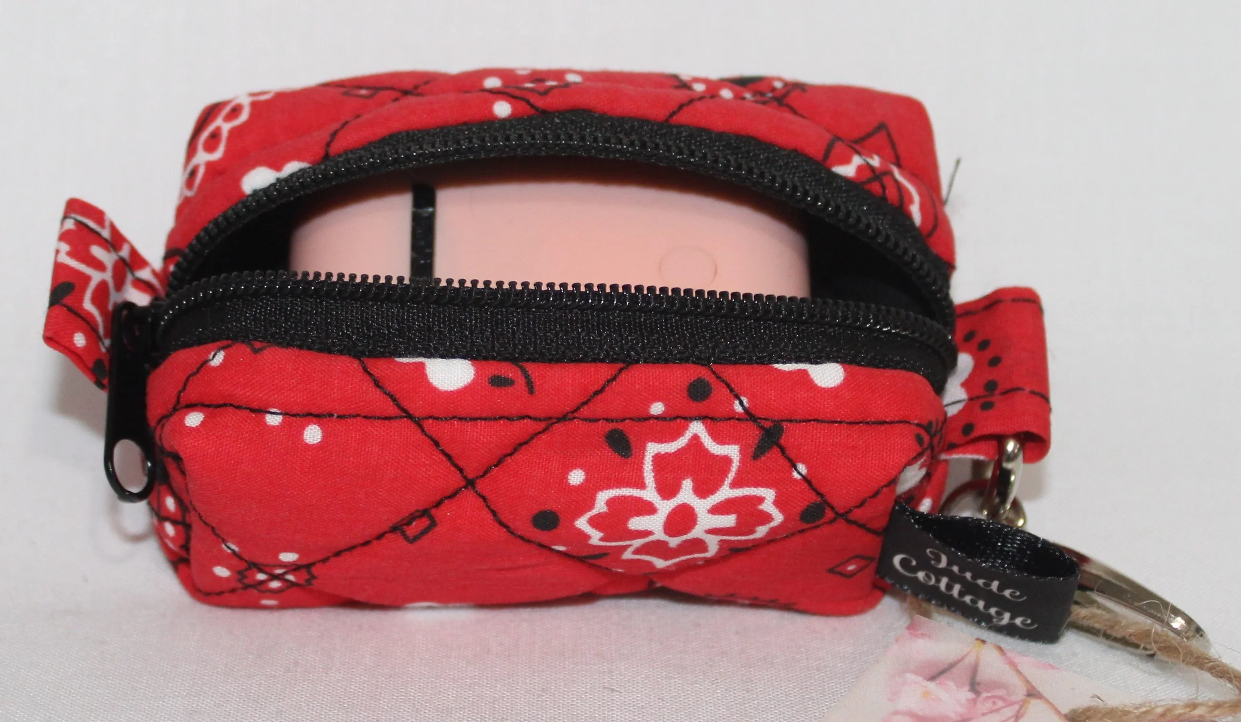 Top open view of the Red Bandana Bag Charm showing bandana print fabric with a set of Airpod earbuds inserted for size reference.