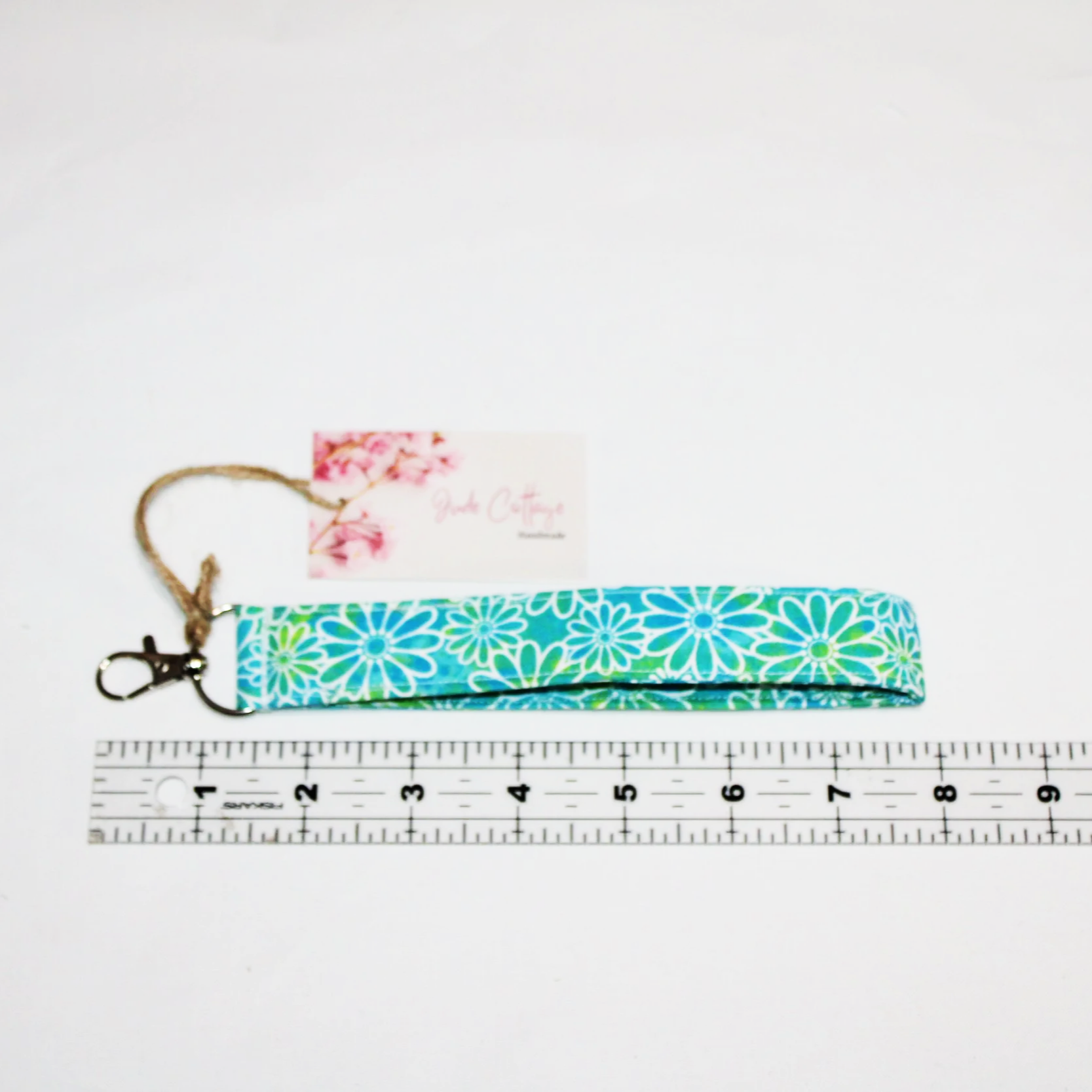 Close-up view of the Neon Daisy wristlet showing the blue and green background with white daisy print placed above a ruler to indicate size.
