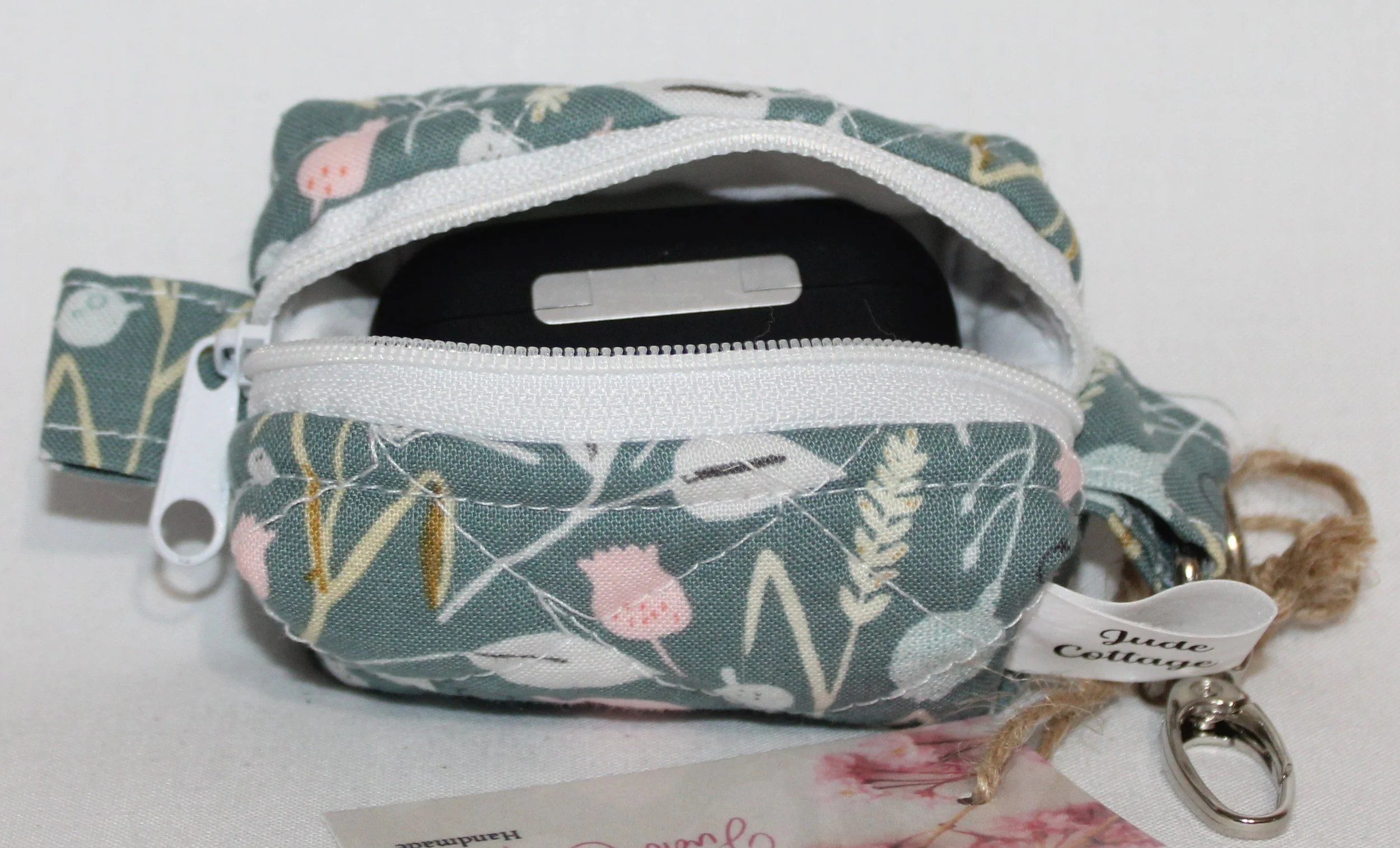 Open top view of the Meadow Breeze Bag Charm featuring a sage green background with spring floral print shown with an Airpod Pro earbud case inserted for size reference.