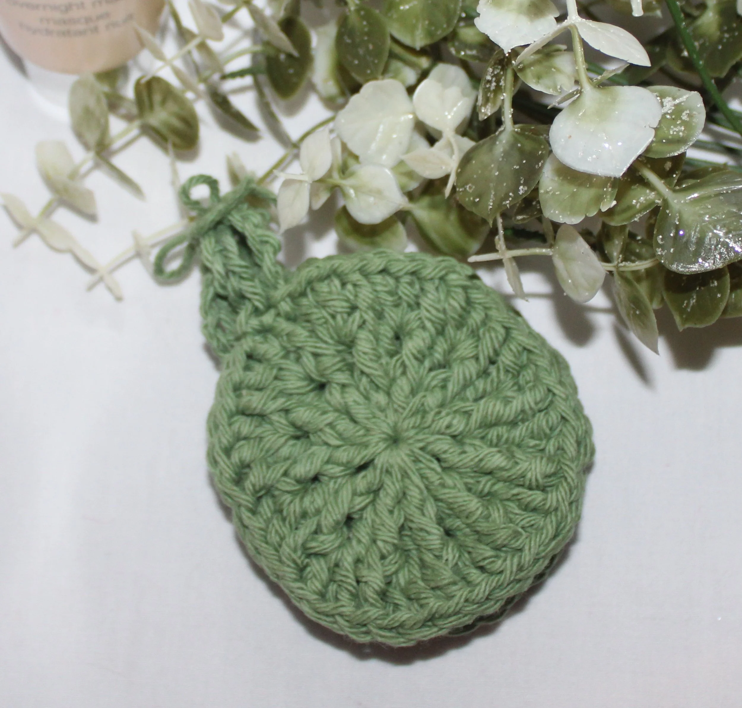 Close‑up of round crocheted sage green facial scrubbies with a textured stitch pattern.