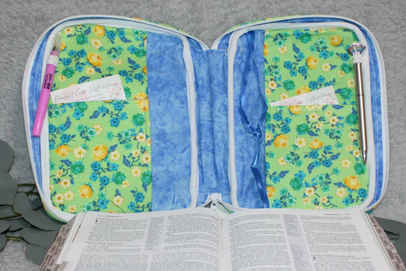 Empty interior view of the Suzanne Study Bible Case, showing the floral lining, interior slip pockets, blue ribbons and pen holders with the case fully open.