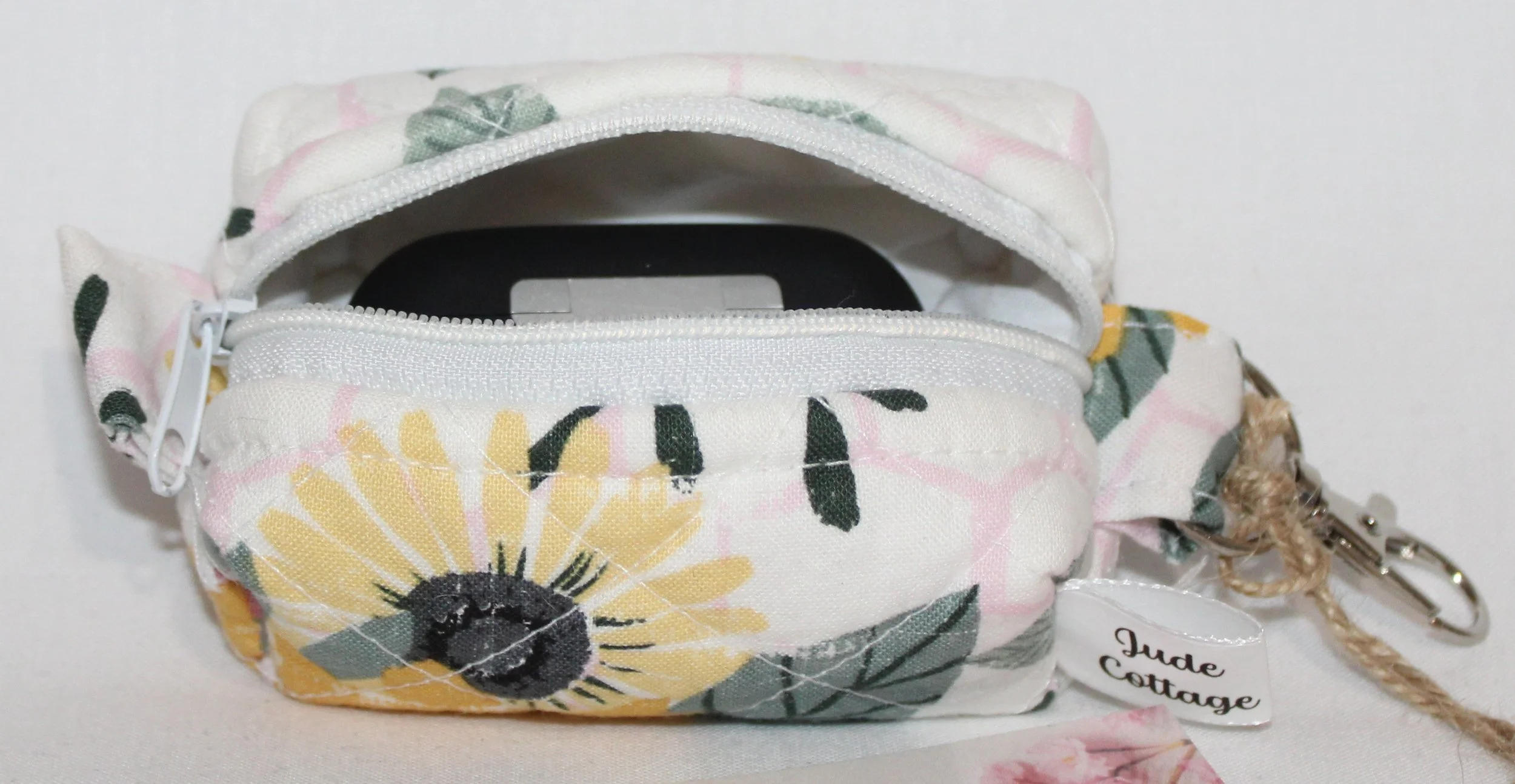 Open top view of the Honeycomb Sunflower Bag Charm featuring a white fabric with pink honeycombs and yellow sunflower print, shown with an Airpod earbud case inserted for sizing reference.