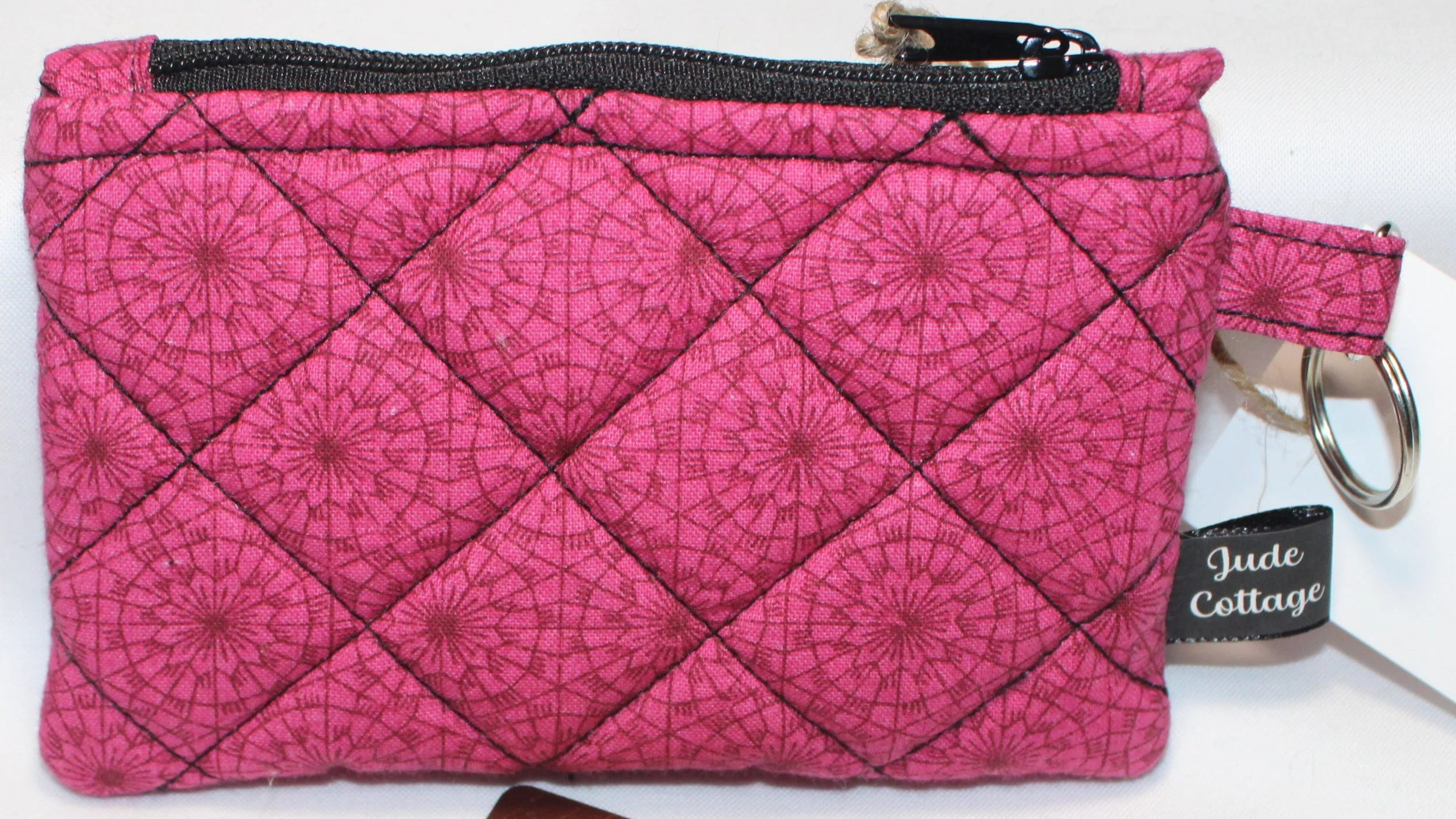 Up-close view of the Clair quilted fuchsia keychain wallet featuring a geometric background, zipper closure and metal keyring for attachment.