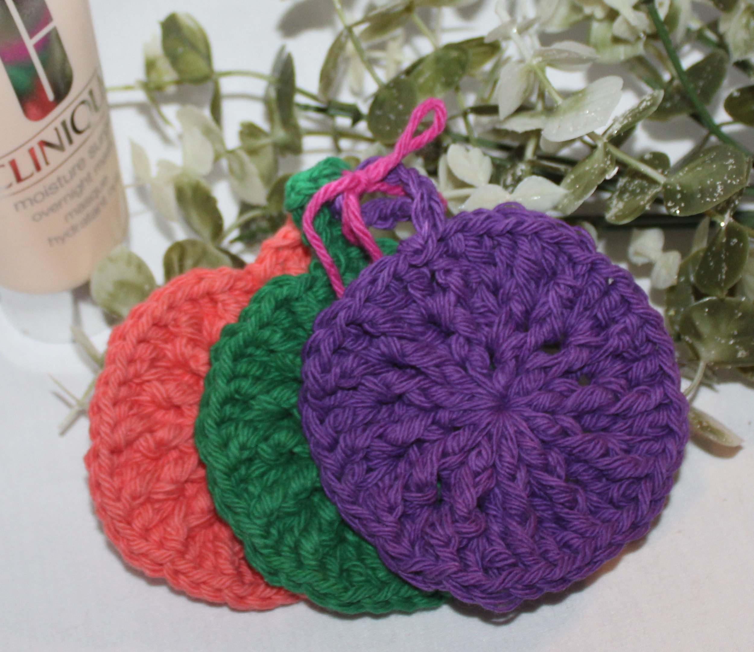 Close‑up of round crocheted assorted colors of green plum coral facial scrubbies with a textured stitch pattern.