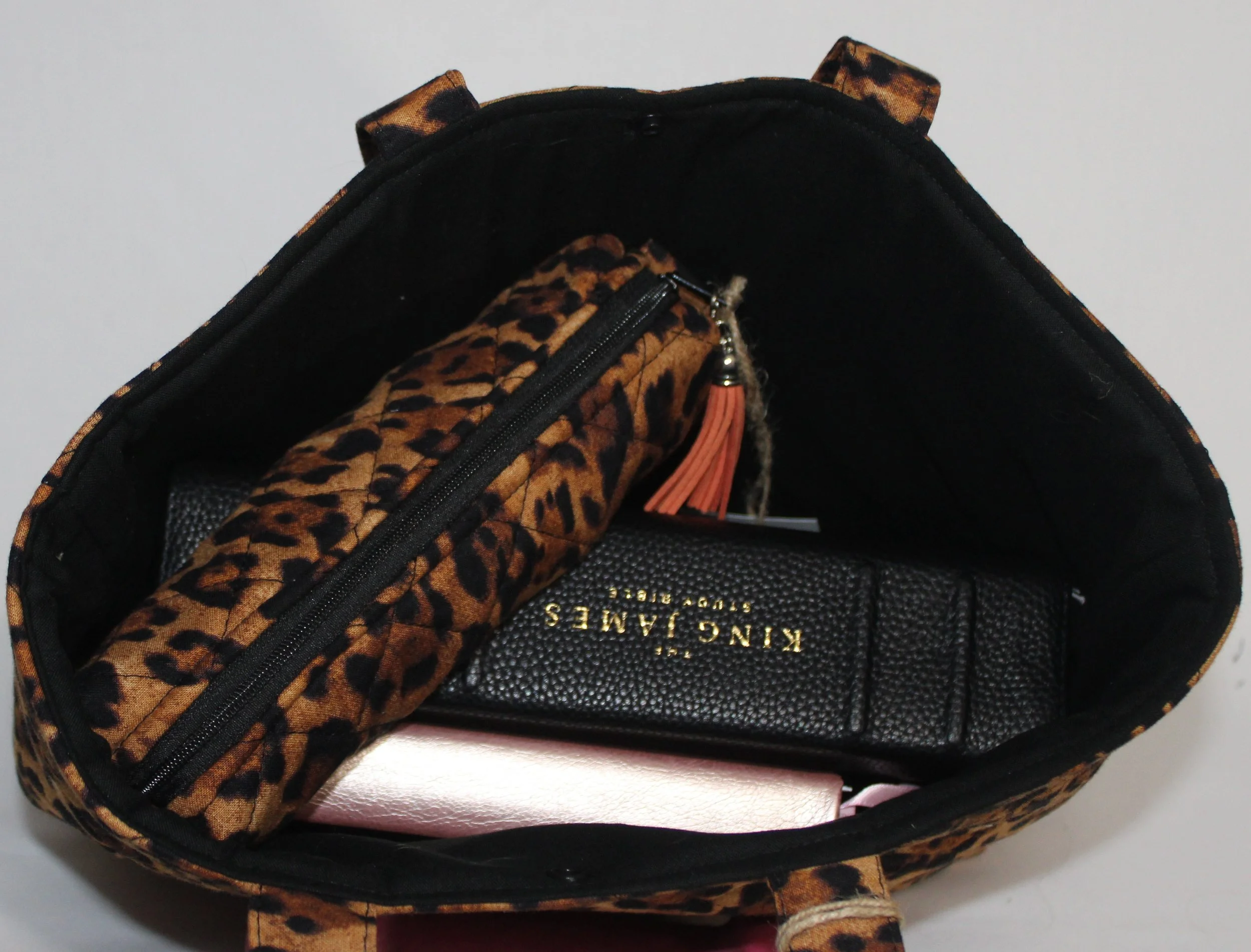 Interior view of the Lyra leopard‑print quilted Bible sleeve shown with a study Bible, pencil pouch, and devotional book inserted to illustrate size and intended use.