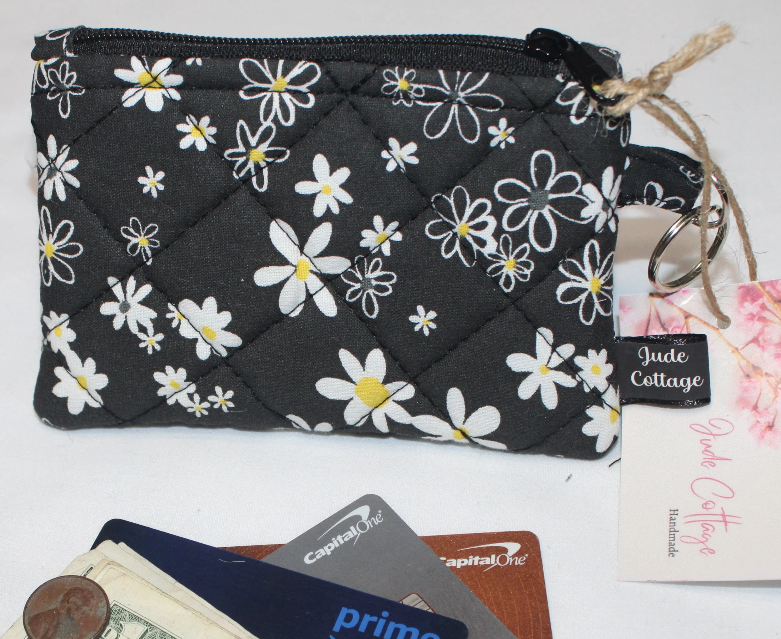 Small zippered keychain wallet featuring white flowers on a black background showing attached keyring.