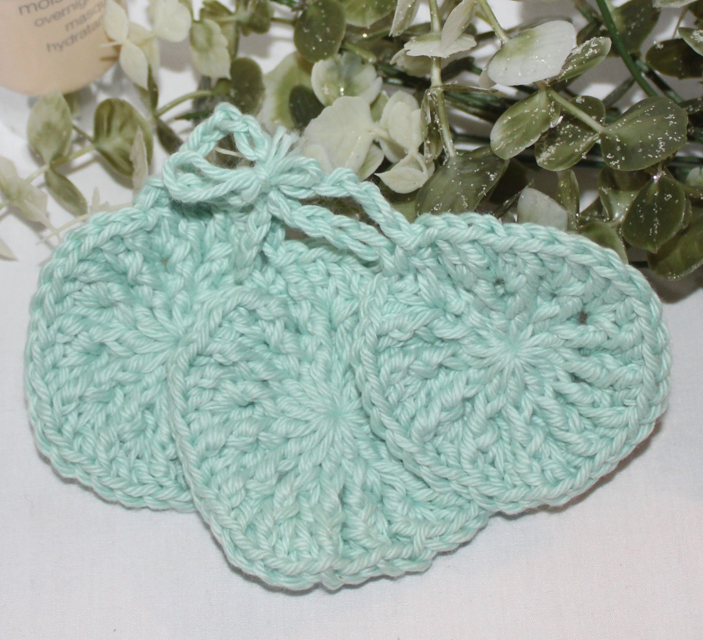Close‑up of set of three round crocheted seafoam facial scrubbies with a textured stitch pattern.