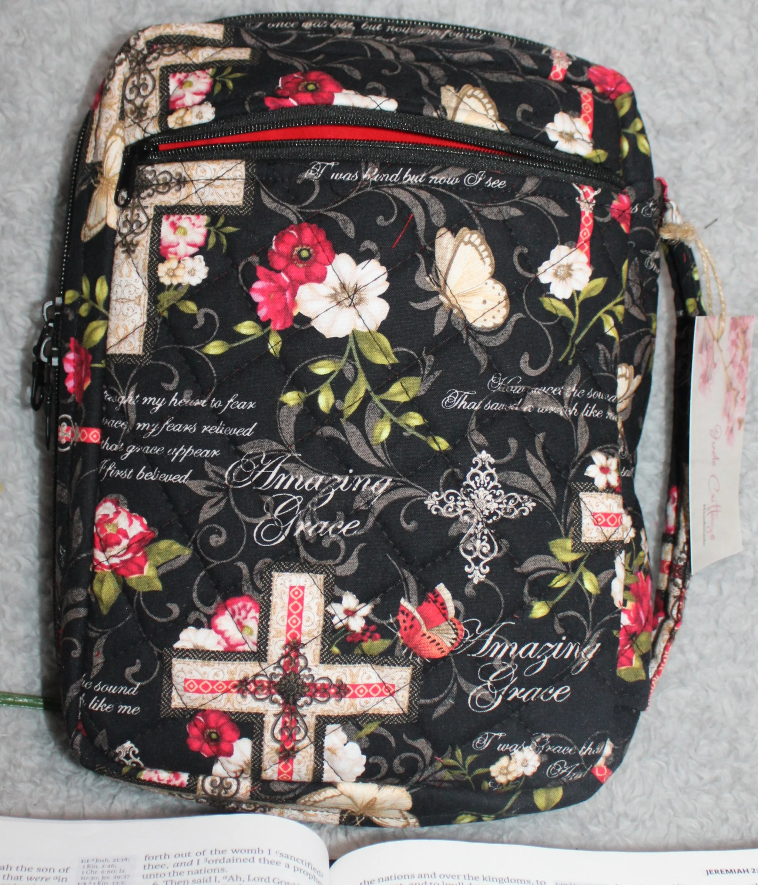 Back view of the Amazing Grace Bible case showing the quilted red and white floral fabric, the exterior zip pocket, and the sturdy padded handle.