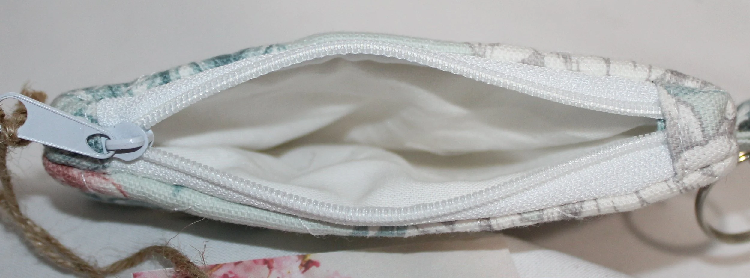 Top view of mint‑green quilted keychain wallet with magnolia floral pattern, zipper closure, and metal key ring.