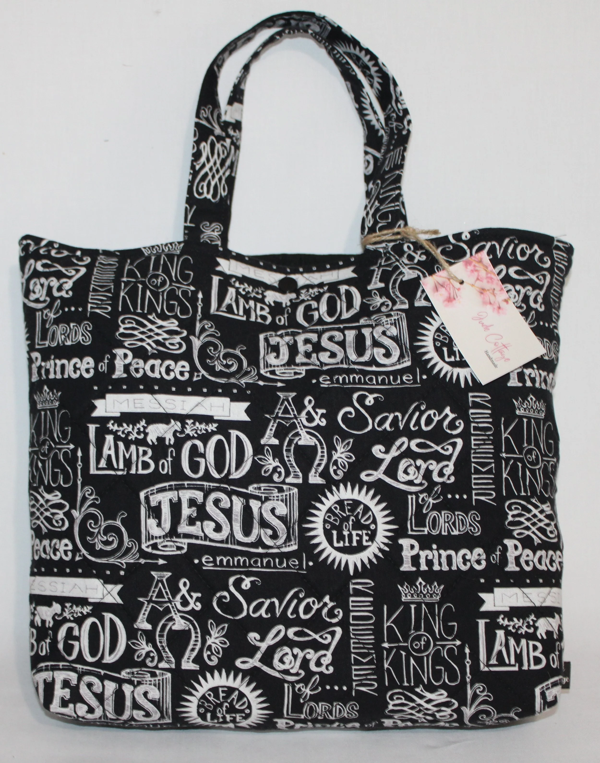 Front view of the King of Kings quilted Bible sleeve with back fabric and white names of Jesus print, showing the two handles and snap closure.