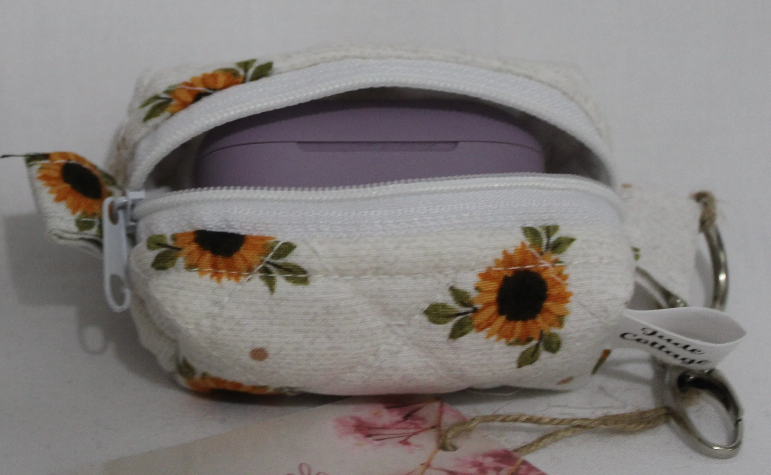Open top view of the Sunflower Medley Bag Charm featuring small sunflowers on a cream background shown with a set of J Lab earbuds inserted for size demonstration..