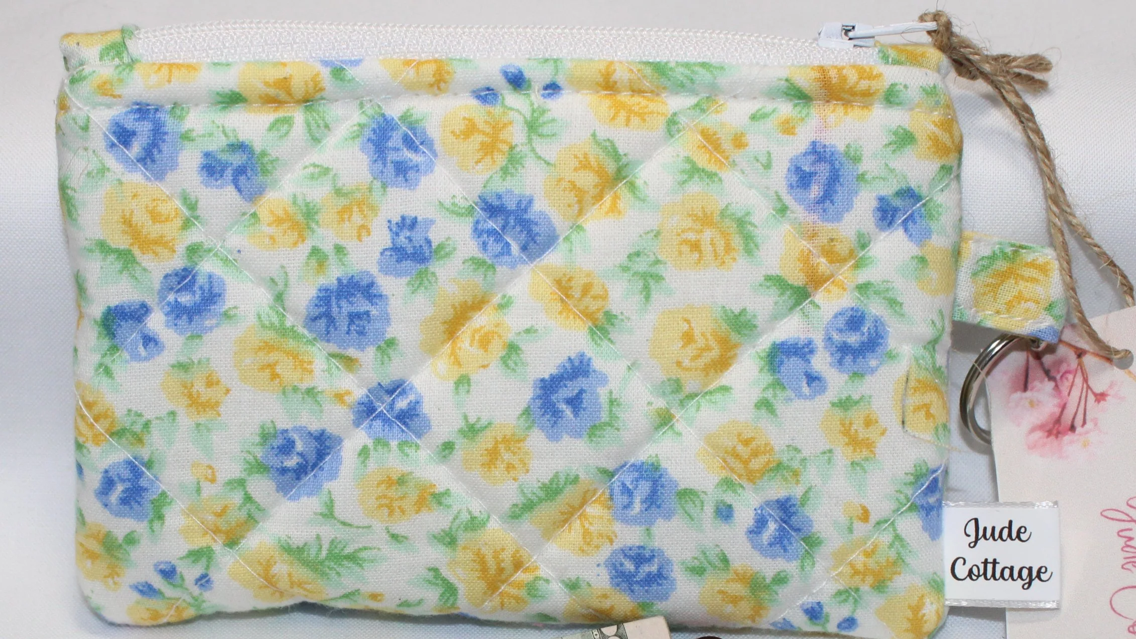 Quilted keychain wallet featuring dainty blue and yellow roses on white background, zipper closure, and metal key ring.