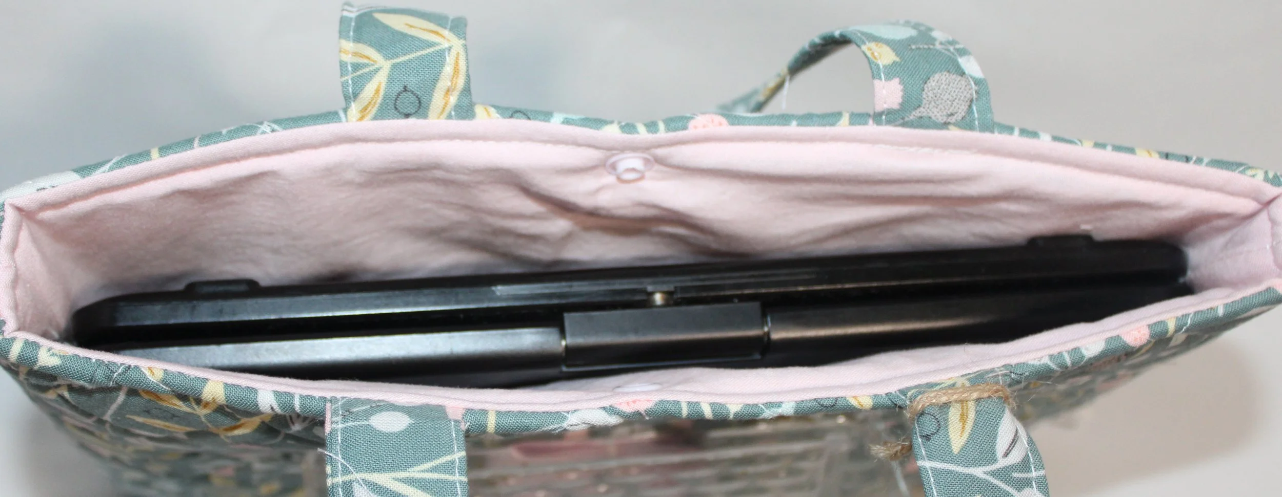 Top view of the Meadow Breeze quilted tablet and book sleeve, showing a tablet inserted and the pink lining visible.