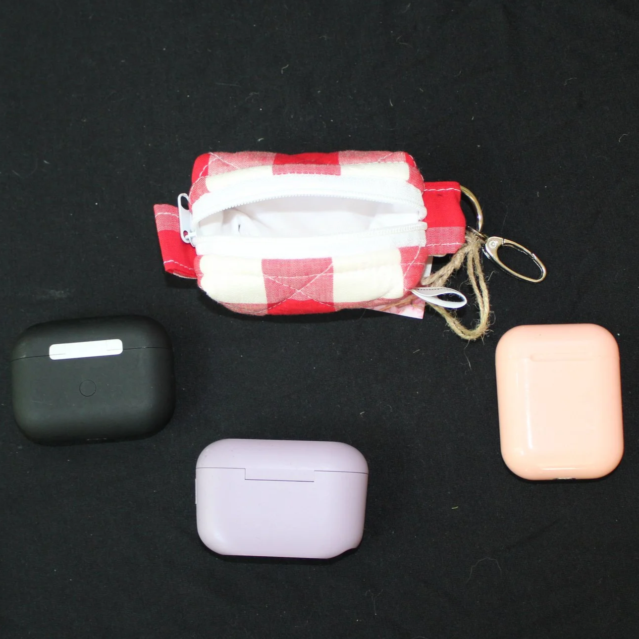 Open top view of the Stella Bag Charm showing white lining and featuring a red and white plaid fabric shown with different sized earbud cases for sizing reference.