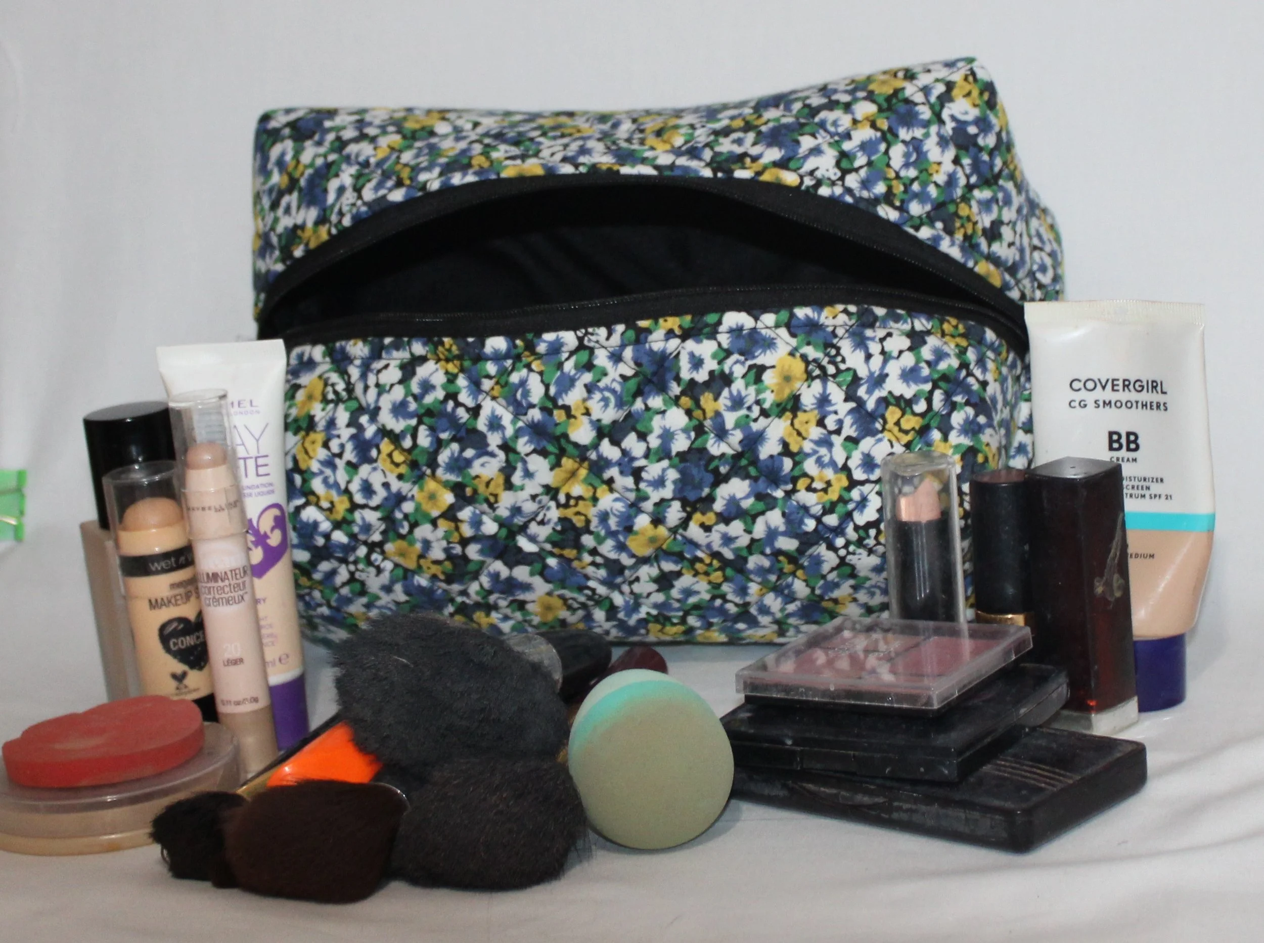 Luna quilted floral travel pouch displayed with assorted cosmetics placed in front, including brushes, makeup items, and skincare products, to show scale.